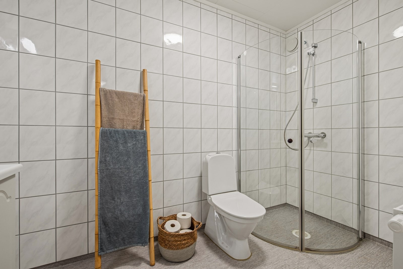 Badet har dusjområde med innfellbare glassdører, gulvmontert toalett og opplegg for vaskemaskin. Galleribilde