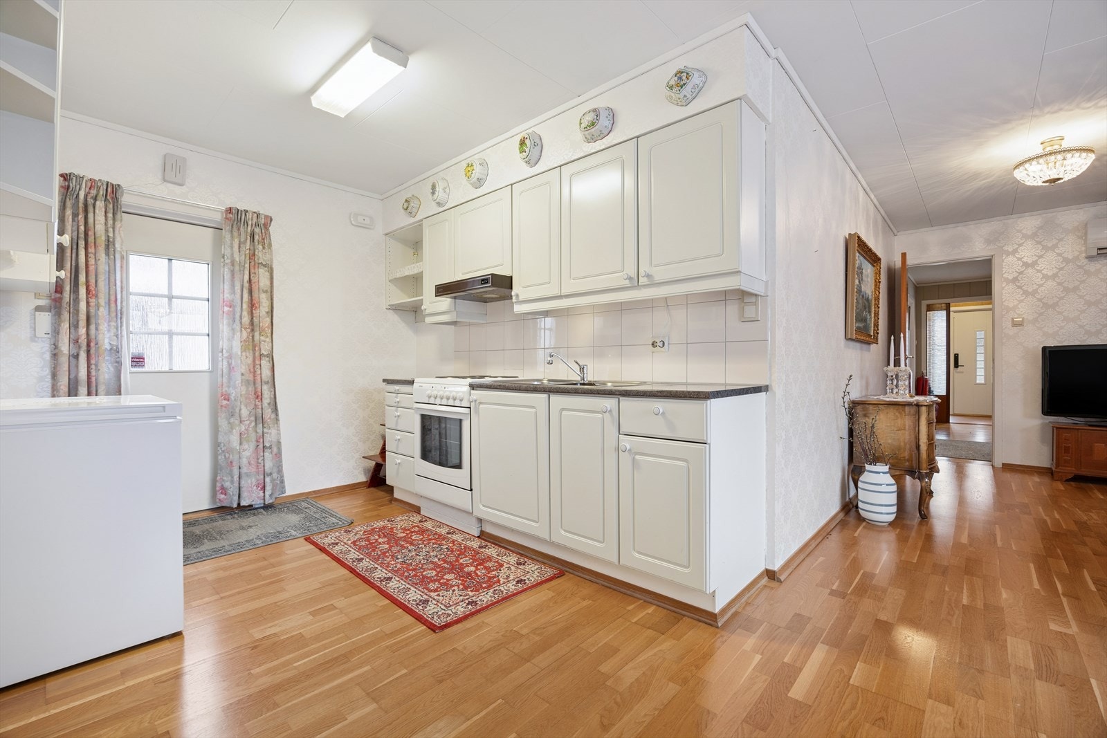 Kjøkkenet i tilbygget er innredet med hvite, profilerte fronter og grå benkeplate i laminat. Også her har man godt med skap- og skuffeplass. Kjøkkenet er i dag utstyrt med fryseboks, komfyr og kjøkkenventilator med avtrekk ut. Galleribilde