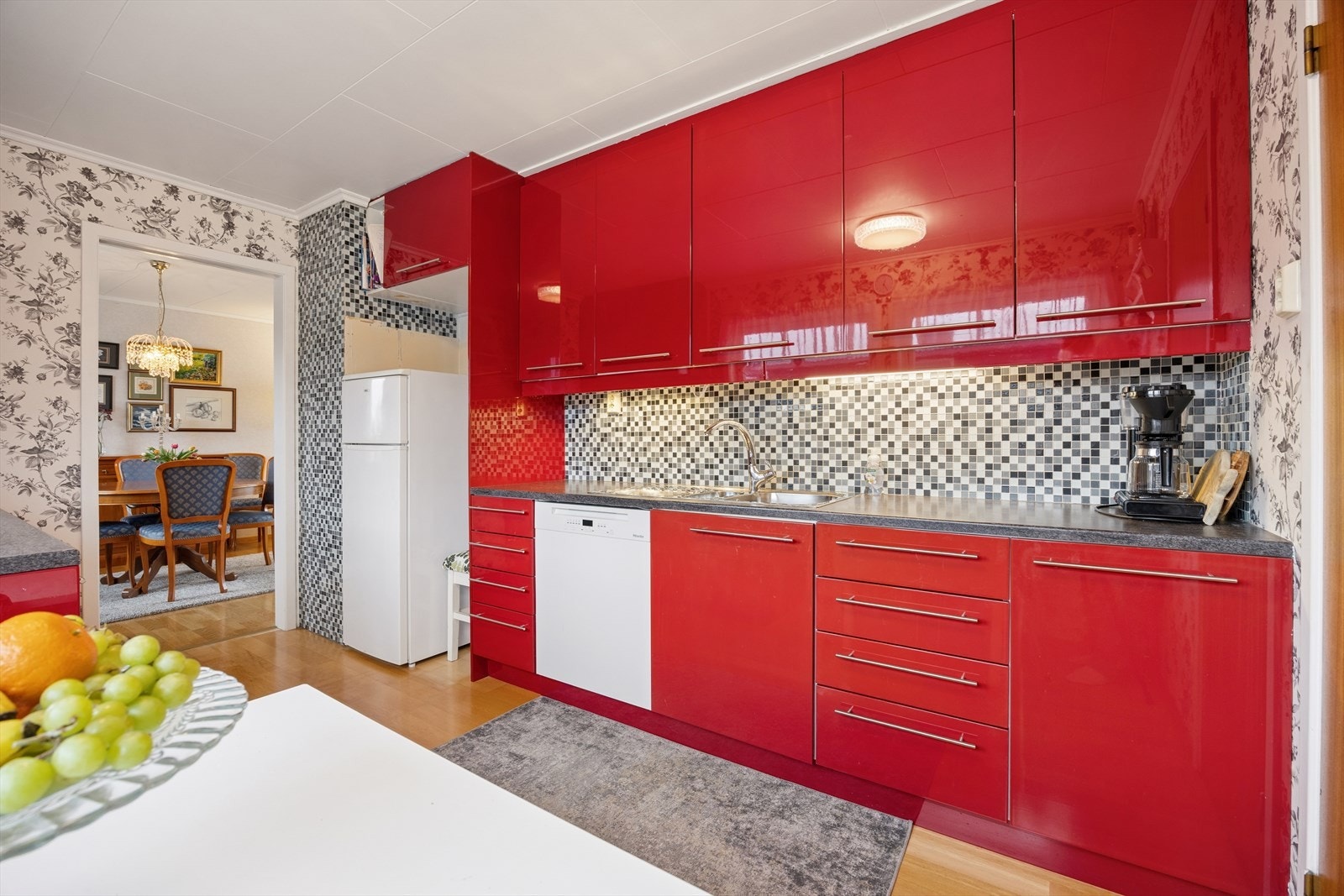 Kjøkkenet er ellers utstyrt med frittstående hvitevarer som kombiskap, oppvaskmaskin, komfyr og kjøkkenventilator med avtrekk ut. Her har man også rom for å møblere med et lite spisebord. Galleribilde