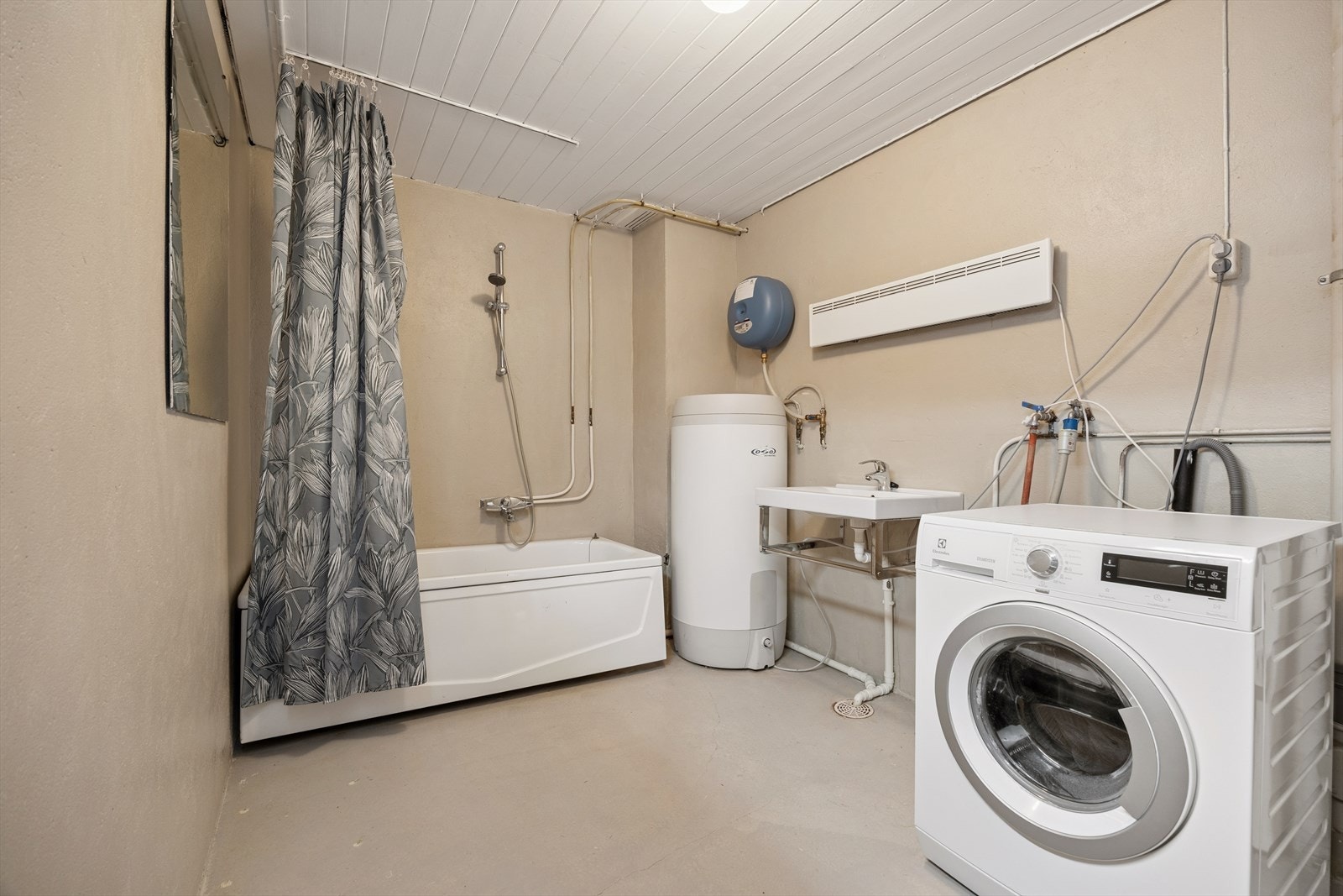 Vaskerommet er innredet med malt betong på gulv og vegger. Rommet er ellers utstyrt med badekar, servant, varmtvannsbereder og opplegg for vaskemaskin. Galleribilde