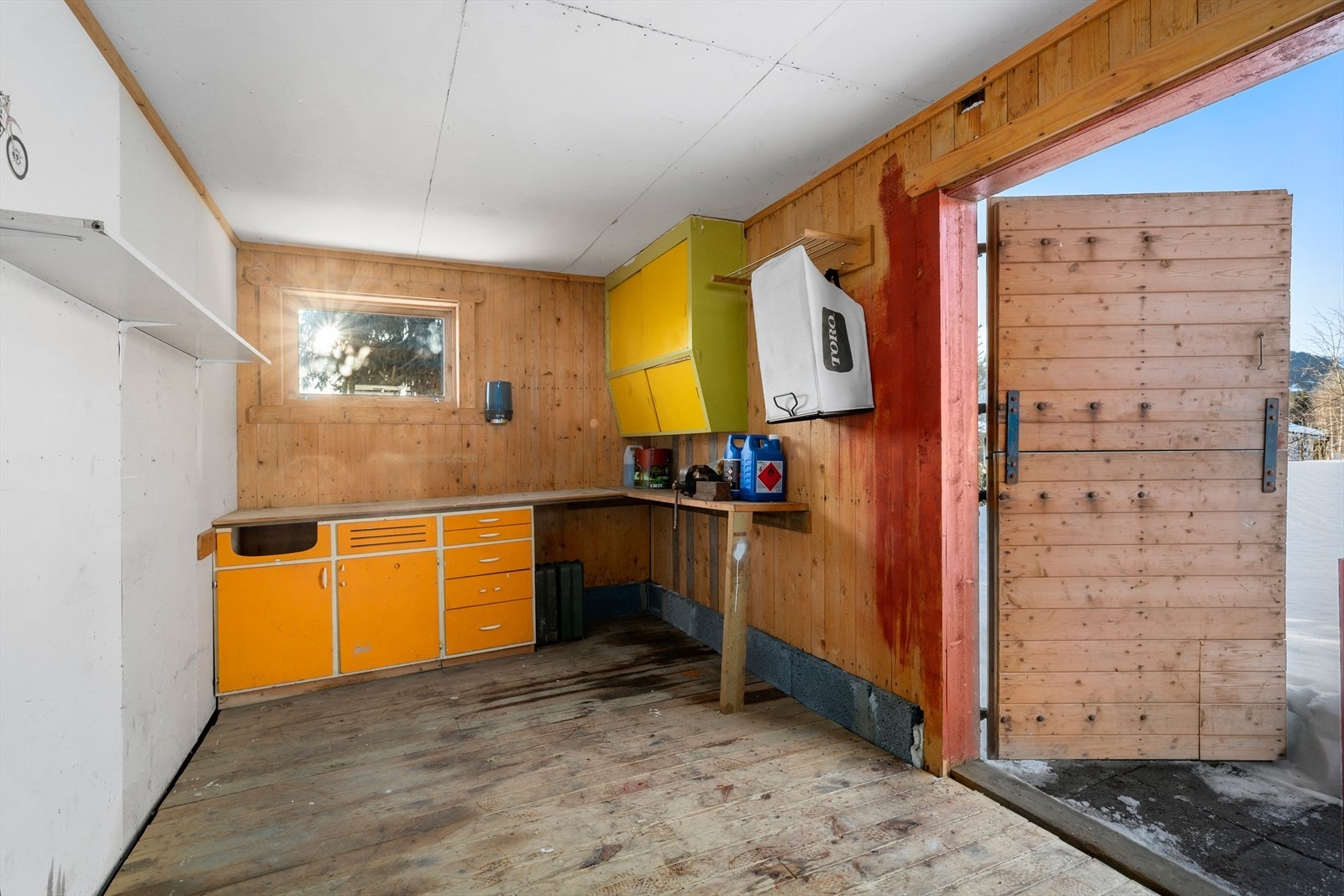 Uthuset har trepanel på veggene og en praktisk arbeidsbenk med skap for oppbevaring. Galleribilde