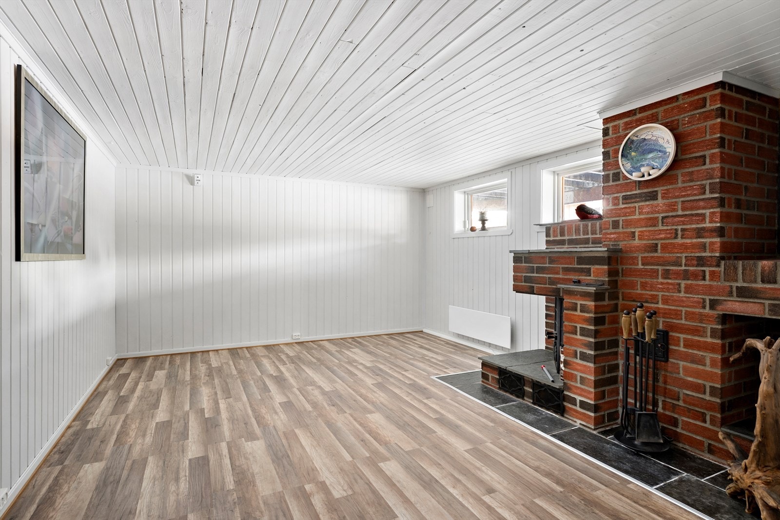 Panelte vegger og tak, samt laminatgulv som gir en robust overflate. Peisen i murstein gir en klassisk varme. Galleribilde