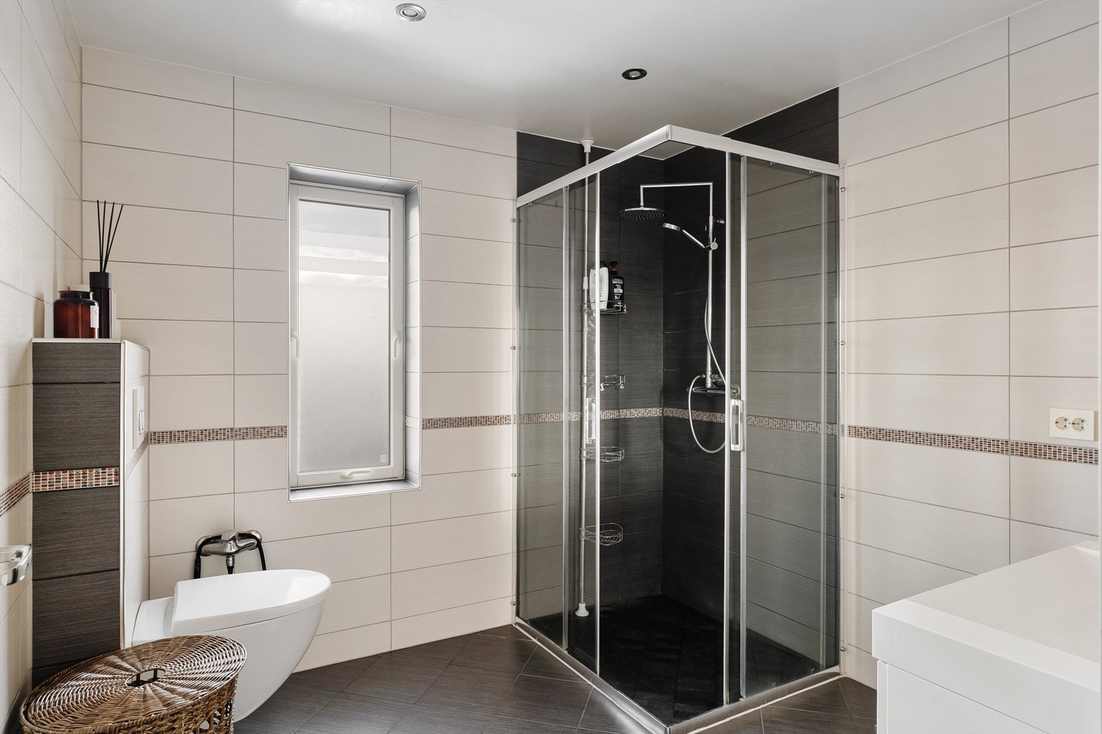 Flislagt bad med dusj, vegghengt toalett og servant i skuffeinnredning. Galleribilde