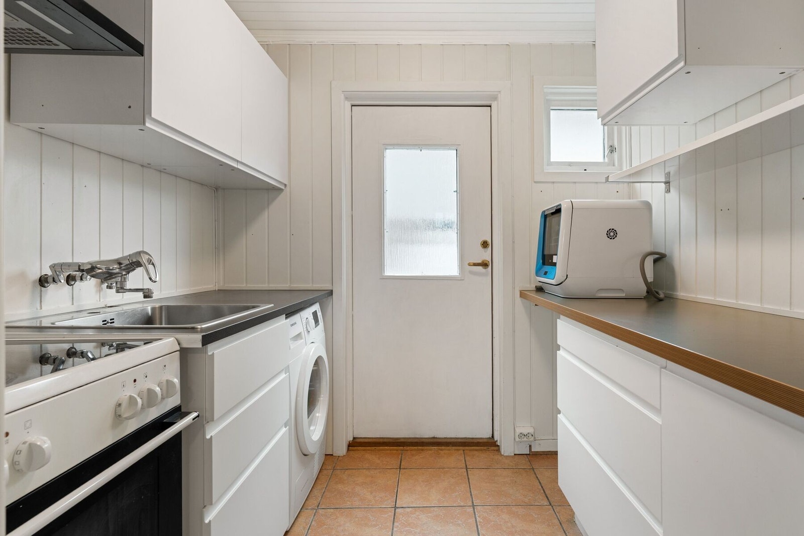 Tidløs innredning fra IKEA med frittstående hvitevarer og opplegg for vaskemaskin. Flislagt gulv med varmekabler. Galleribilde