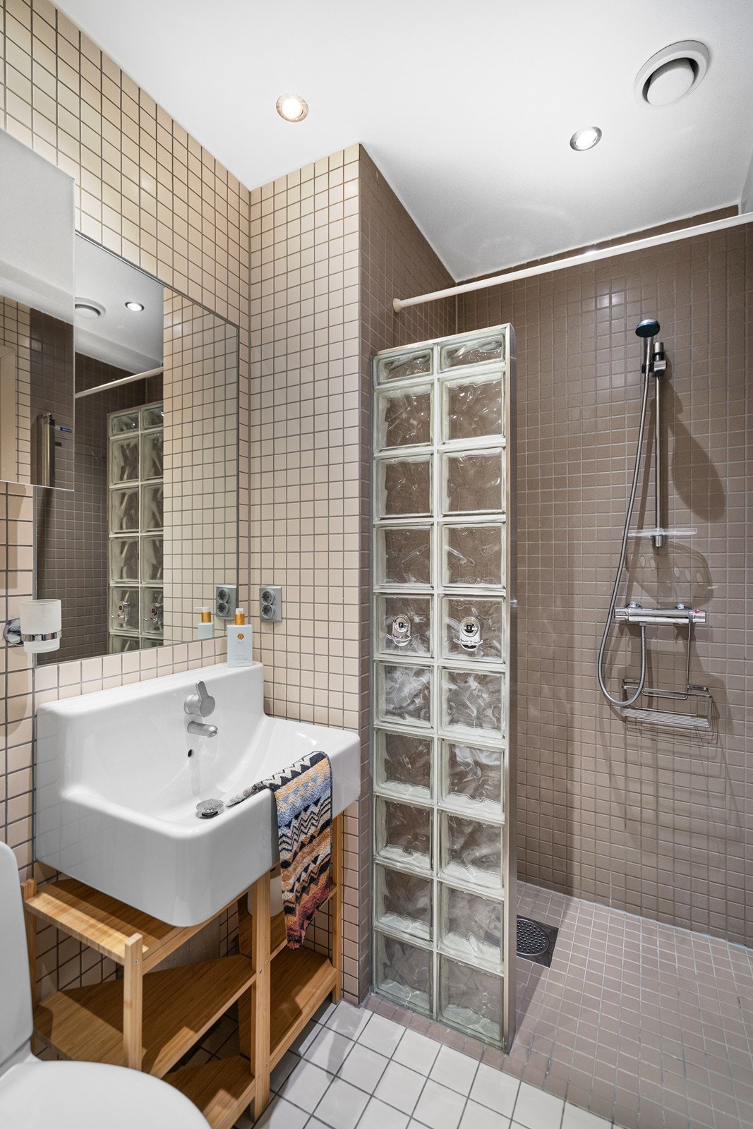 Rommet er innredet med servant, speil med overlys, praktisk oppbevaring under vasken, toalett og et funksjonelt dusjhjørne som utnytter plassen på en effektiv måte. Galleribilde