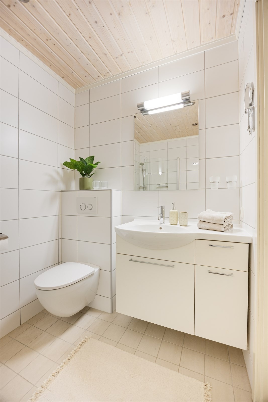 Badet innehar veggmontert toalett, dusjnisje med glassdører og servantinnredning med skap, skuff og speil med overlys. Galleribilde