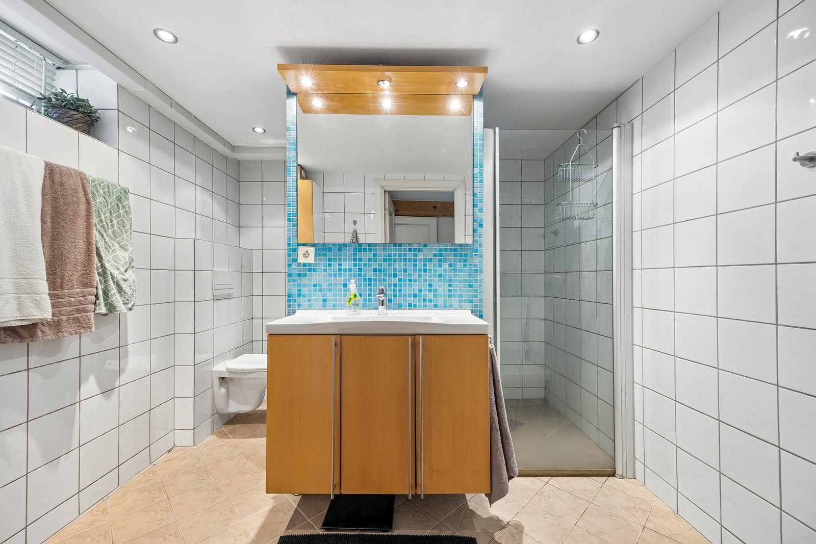 Badet har flislagte overflater og er utstyrt med dusj, servantinnredning og toalett. Galleribilde