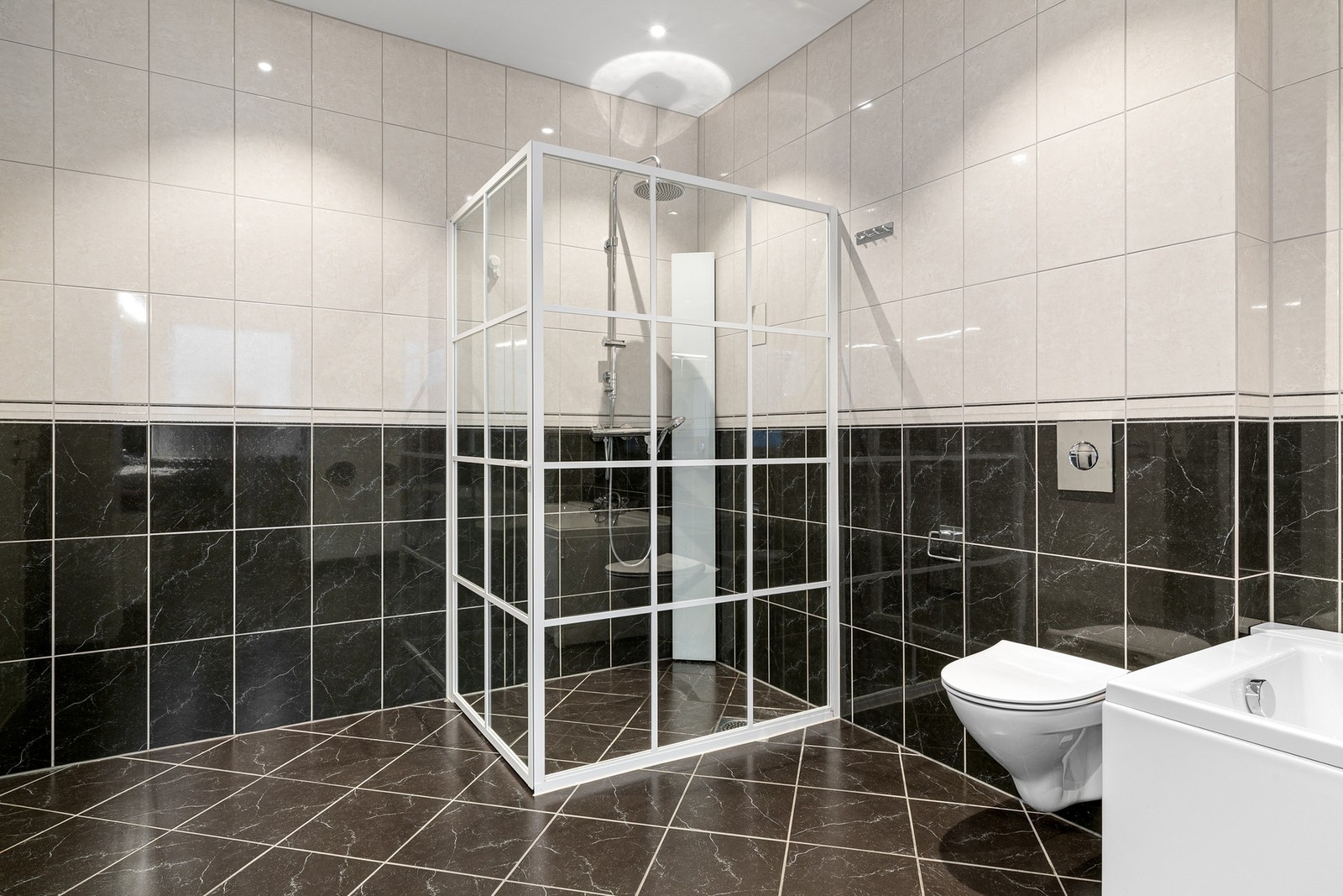 Badet er helfliset med gulvvarme og innredet med dobbelt servantskap, høyskap og speilskap. Videre er rommet utstyrt med badekar, dusj og toalett. Galleribilde