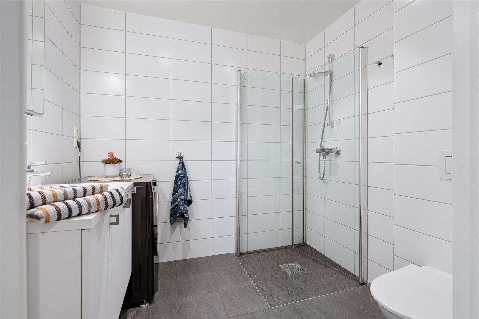 Helfliset baderom med spotter i tak, vegghengt toalett, dusjhjørne og opplegg for vaskemaskin Galleribilde