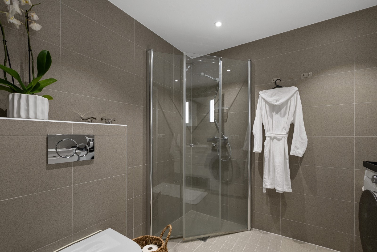 Badet har praktisk innredning med skap og glatte fronter, servant, veggfestet toalett og dusj på gulv. Galleribilde