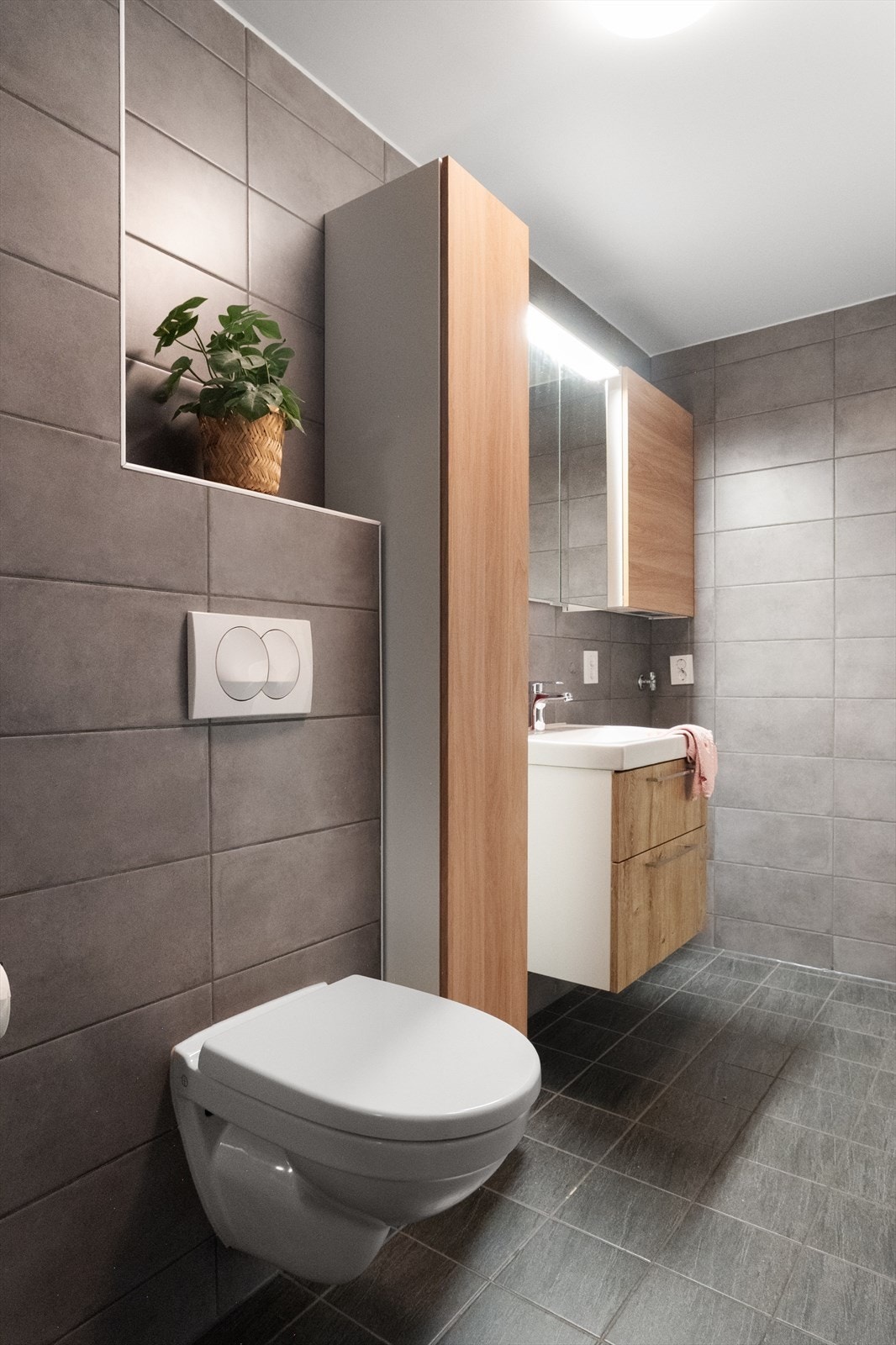 Badet er innredet med dusjhjørne, vegghengt toalett, hvit vask med skapinnredning samt overskap med speilfronter og lys. Galleribilde