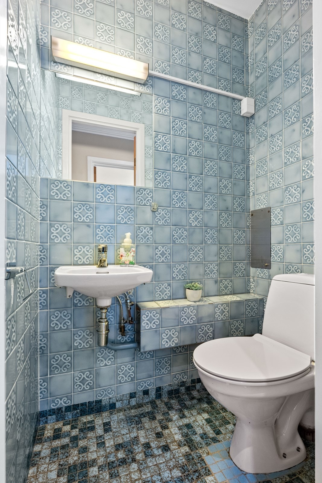 Toalettrommet har montert klosett og servant. Fliser på gulv og vegger. Galleribilde