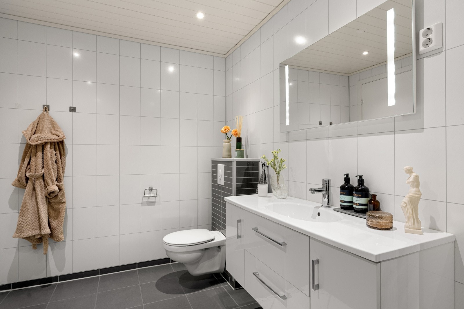 Badet er flislagt med spotter i taket, varmekabler i gulvet og speilet har integrert belysning. Galleribilde