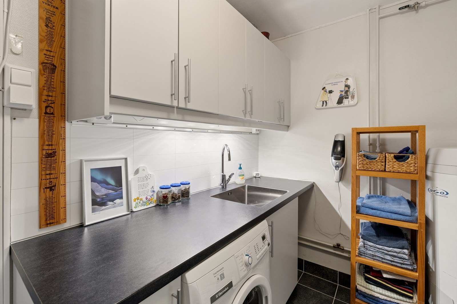 Praktisk vaskerom med flislagt gulv med varme, utslagsvask og opplegg for vaskemaskin. Galleribilde