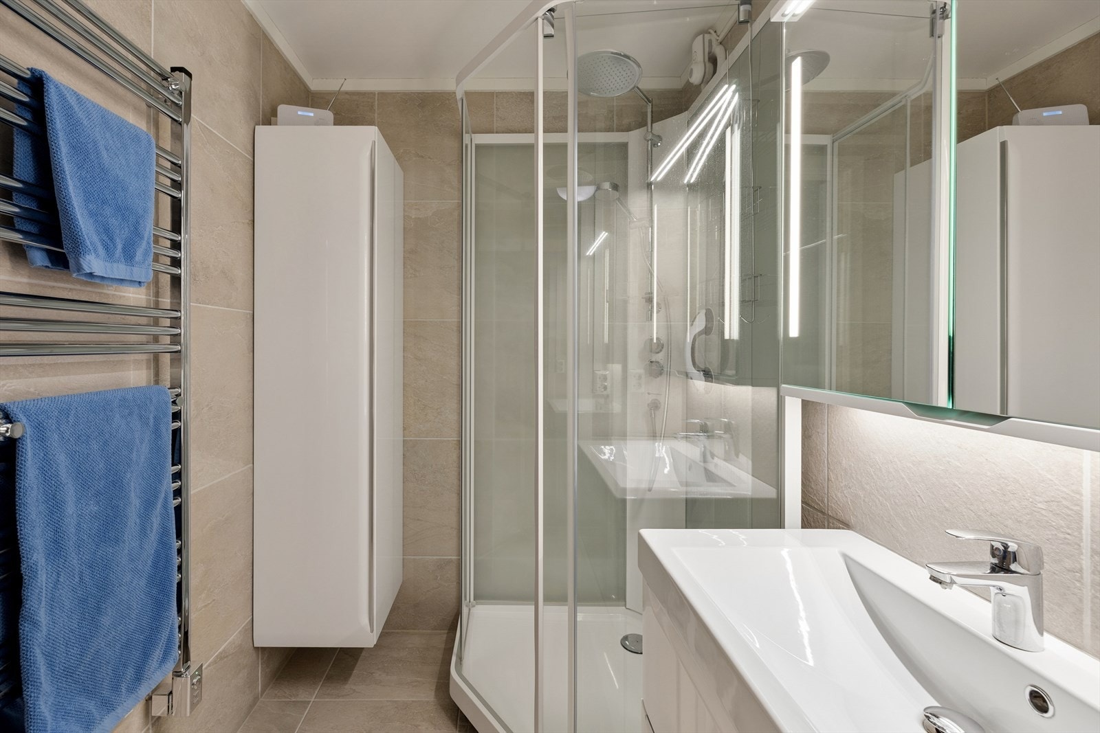 Badet ble oppgradert i 2019 med fliser på gulv og vegger. Rommet er utstyrt med dusjkabinett, håndklevarmer, veggskap, innredning med servant, samt speilskap. Galleribilde