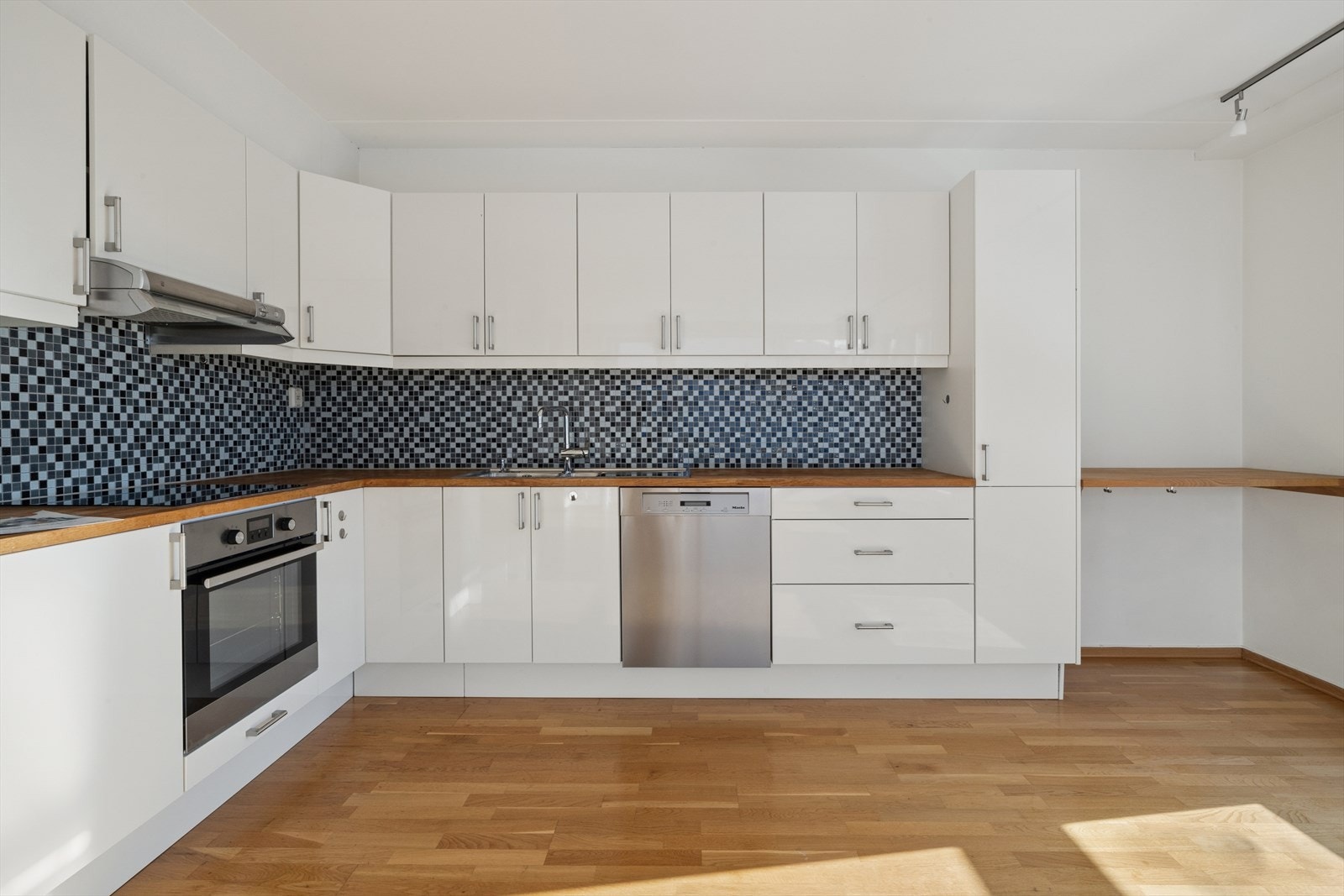 Kjøkkeninnredning med hvite høyglansfronter og benkeplate i tre. Galleribilde