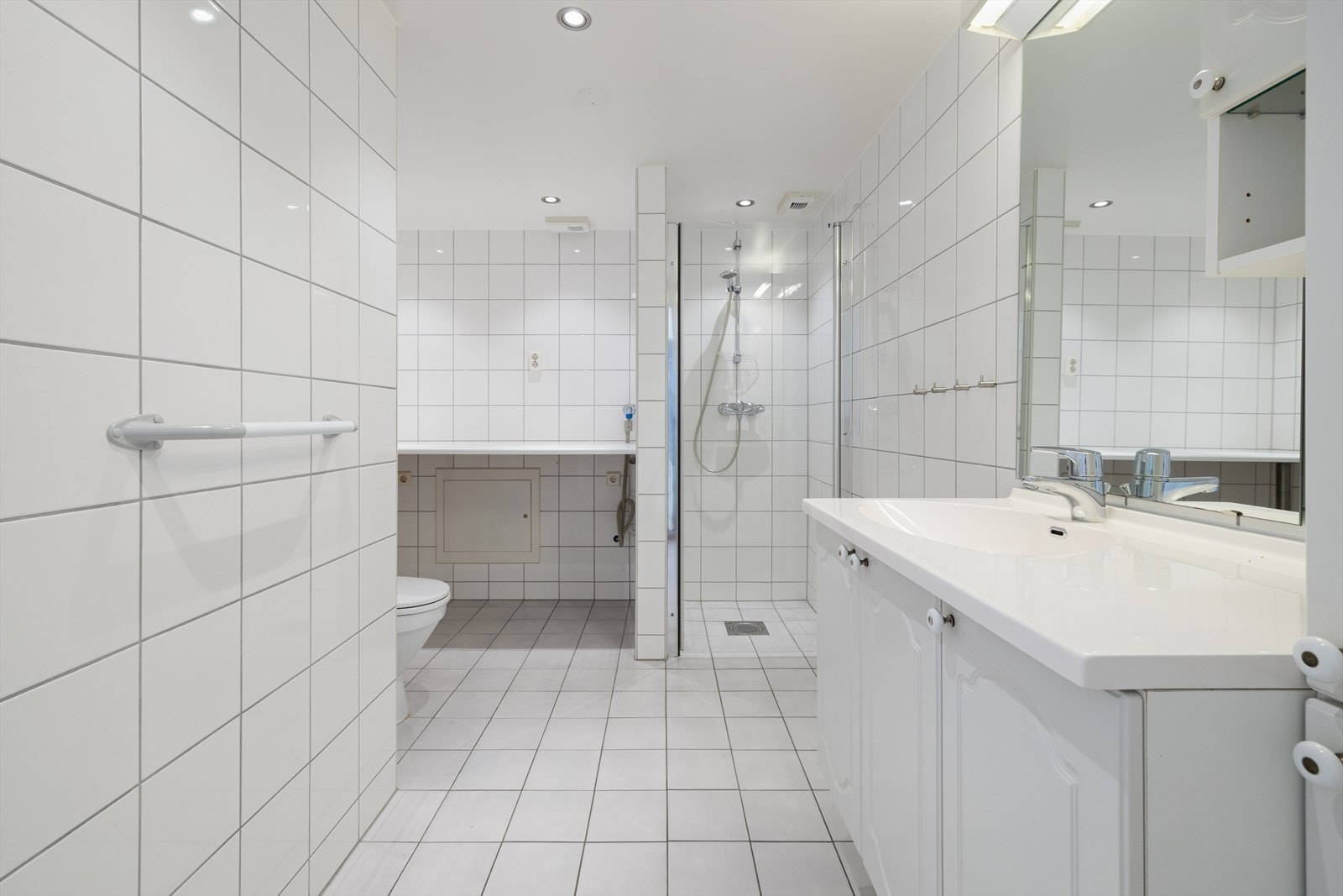 Flislagt bad med varmekabler i gulvet, dusjnisje og opplegg for vaskemaskin. Galleribilde