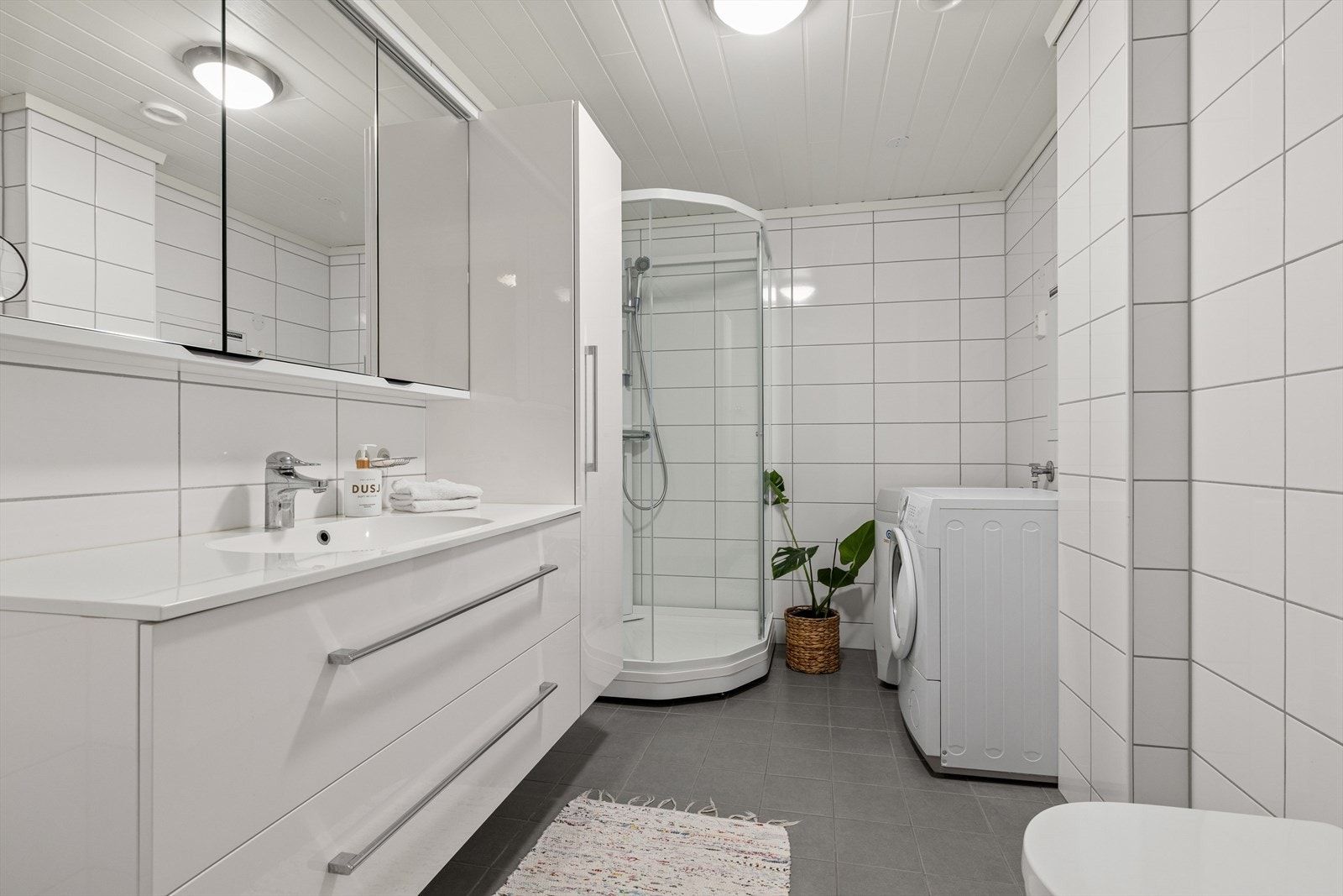Leiligheten har et flislagt baderom med dusjkabinett og opplegg for vaskemaskin. Galleribilde