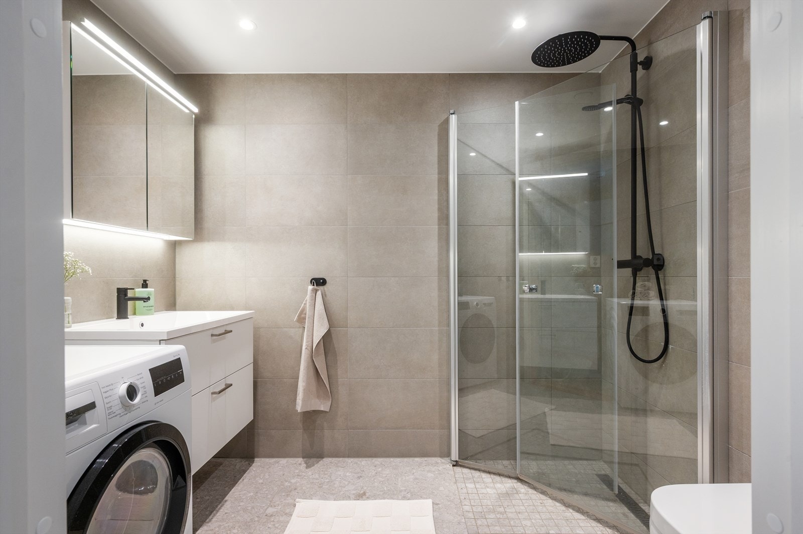 Pent bad med vegghengt toalett, servant med innredning og speil med lys. Galleribilde