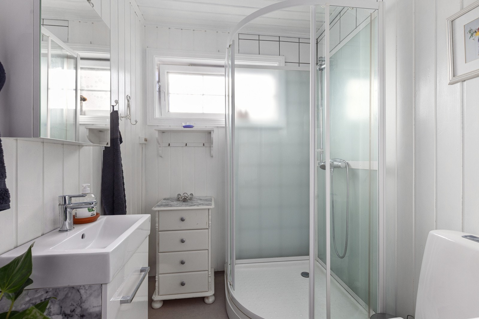 Lyst bad med toalett, dusjkabinett, servant med skuffer og speilskap Galleribilde