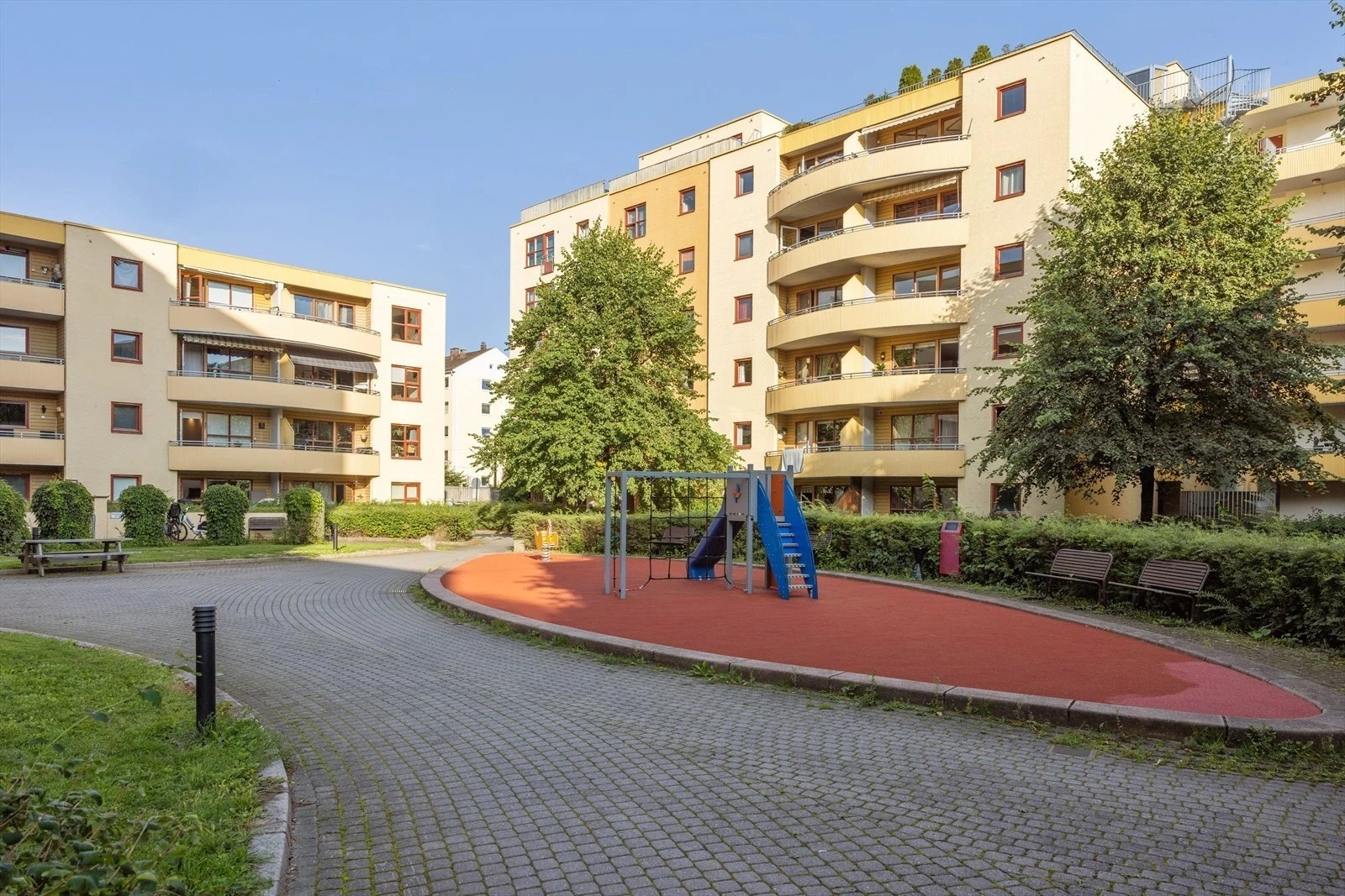 Skjermet og trafikkfri bakgård med plen, variert vegetasjon, lekeapparater og gangveier med belegningsstein. Galleribilde