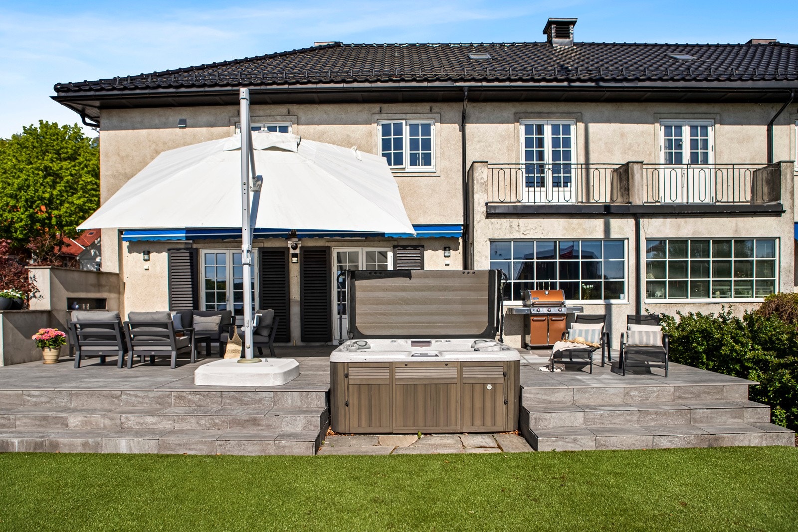 Det er montert både markiser og utebelysning på husveggen, og det er adkomst fra hage, stue og gårdsplass. I hagen rammes plenen inn med bed, hekk og en lav vegg i mur, og det er satt opp en flaggstang som er med på å understreke idyllen ytterligere. Galleribilde