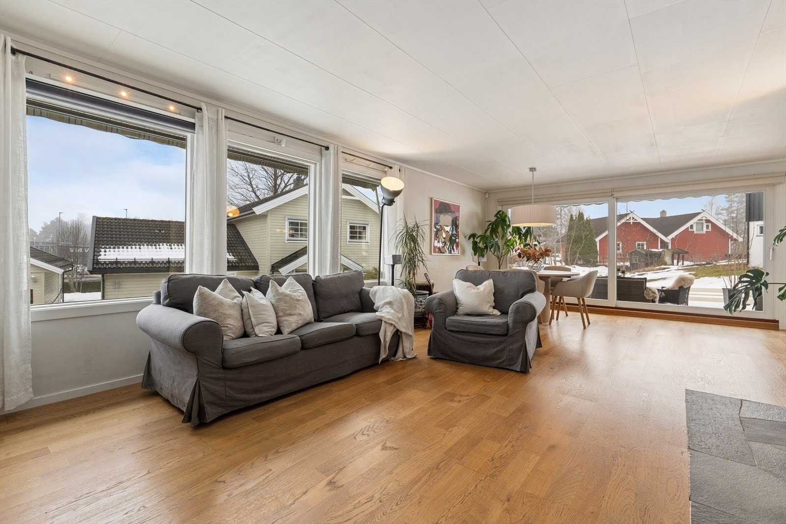 Store vindusflater skaper en åpen og lys atmosfære i stuen. Det er motorisert persienne over vinduene i stuen. Galleribilde