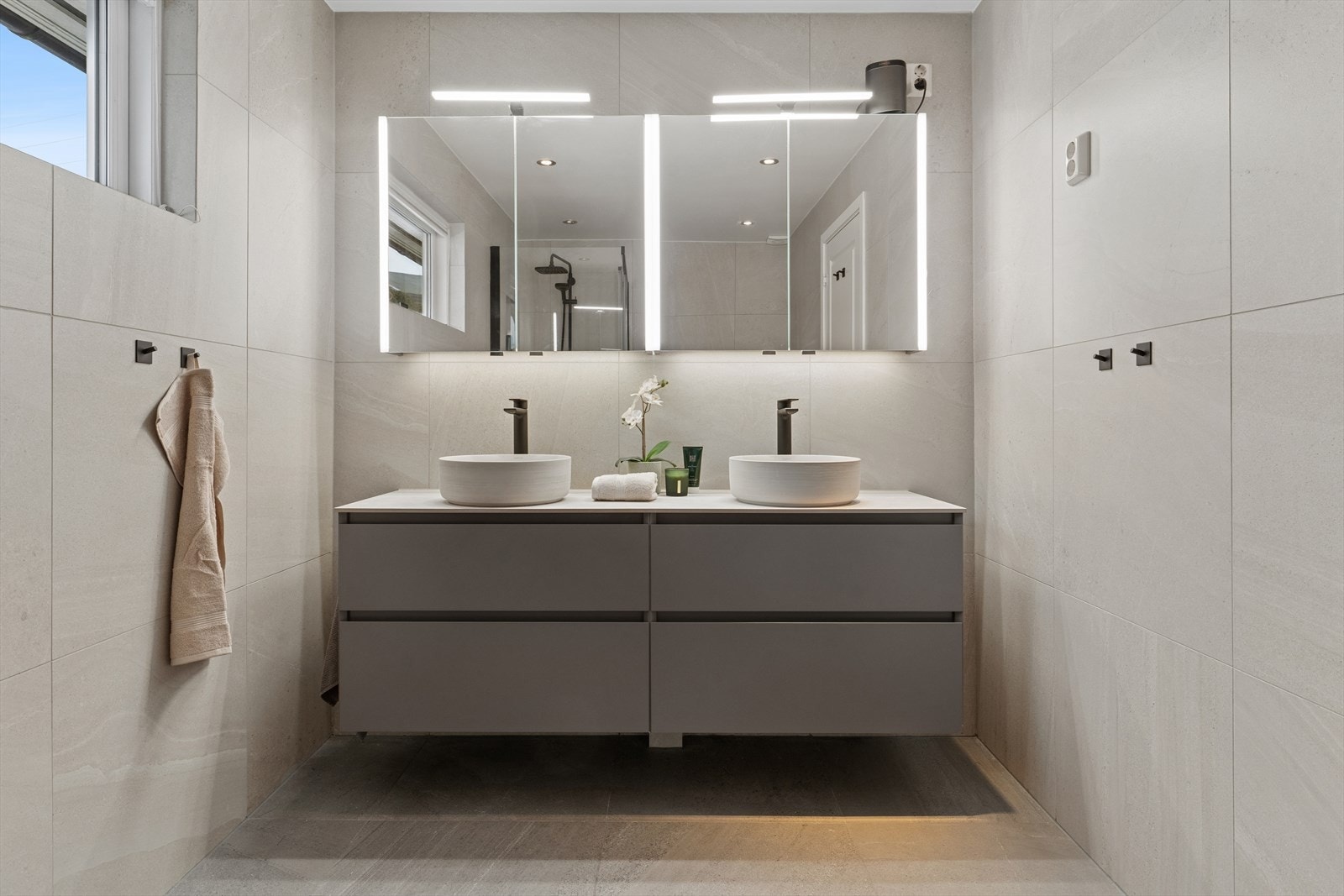 Badet er flislagt med varme i gulv. Dobbelt servantskap med to overliggende servanter og ett-greps armaturer. Galleribilde