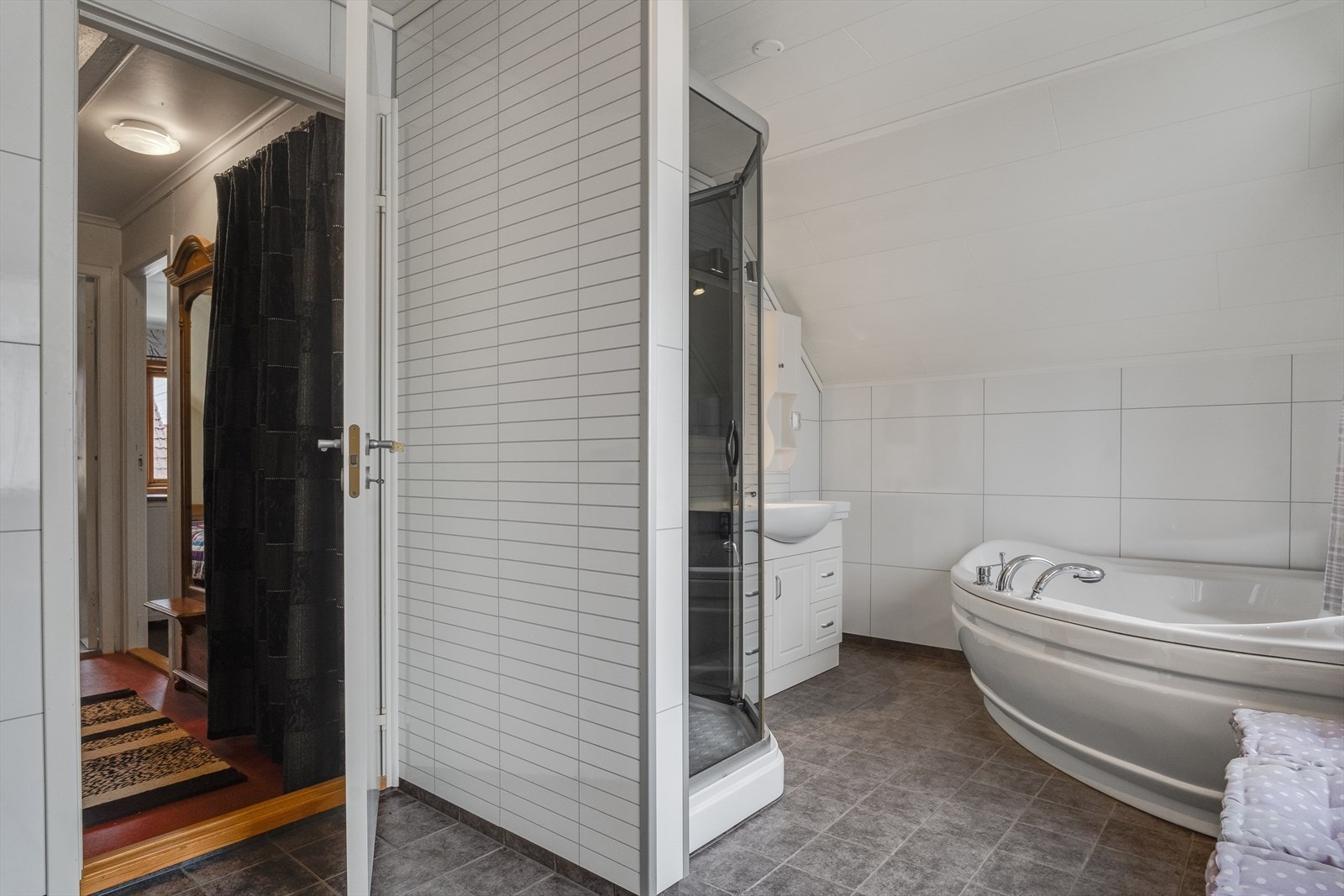 Stort baderom med fliser på gulv og baderomsplater på vegg, utstyrt med både dusjkabinett og badekar. Opplegg for vaskemaskin. Galleribilde