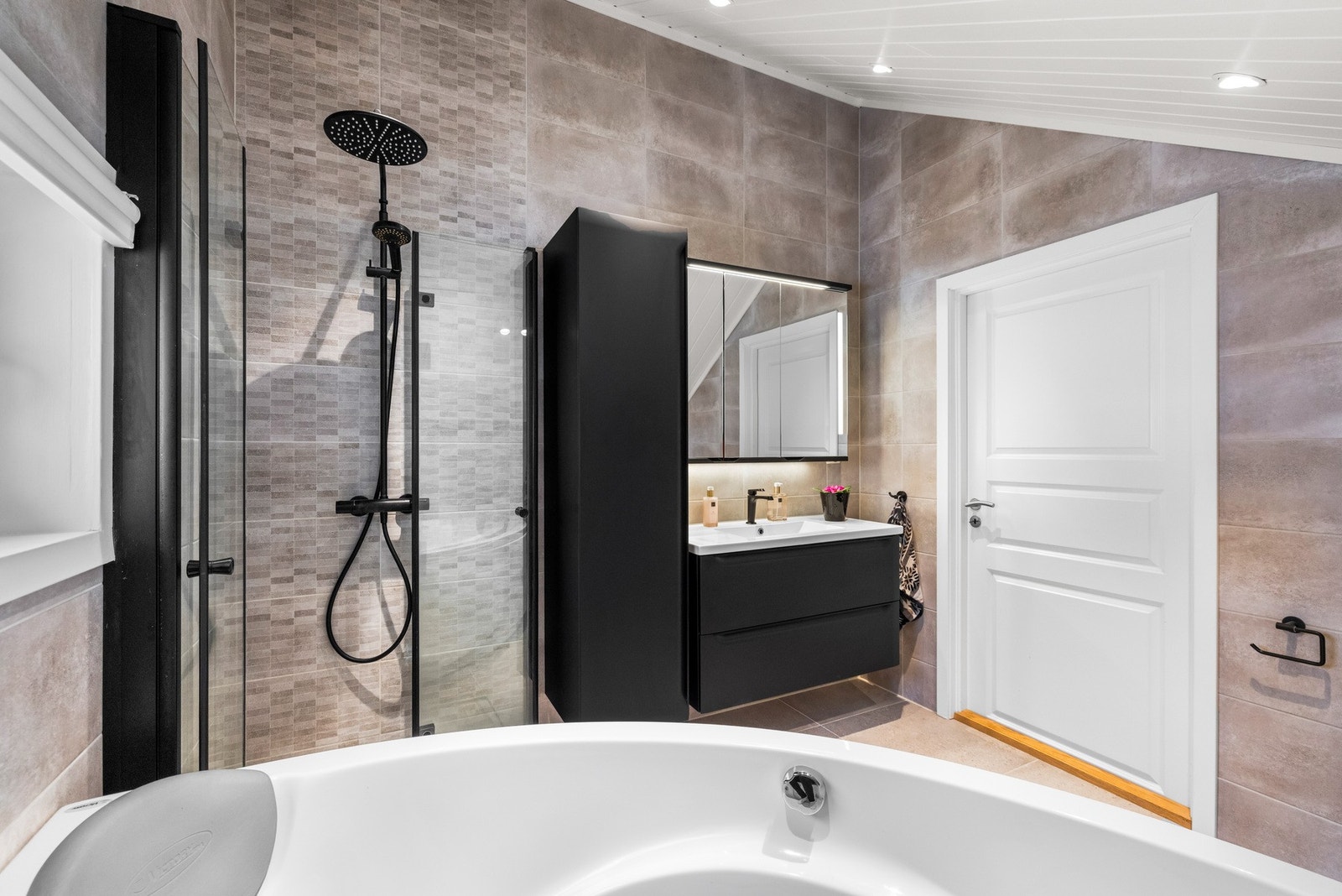 Veggene er flislagt i en lun beige fargetone, mens skråtaket er kledd med malte plater og utstyrt med downlights som gir god belysning. Galleribilde