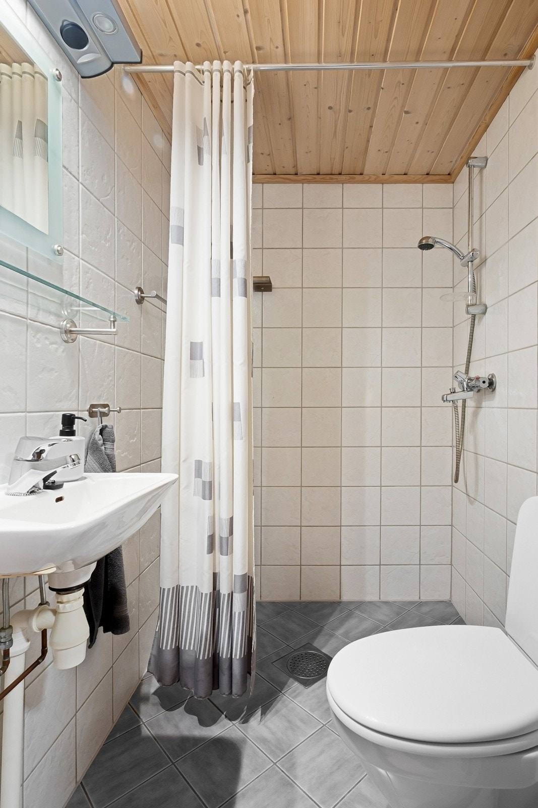 I kjelleren er et flislagt bad med ukjent alder. Badet har flislagte vegger og gulv, himling med trepanel, dusjnisje med forheng, veggmontert servant og gulvfestet toalett. Galleribilde