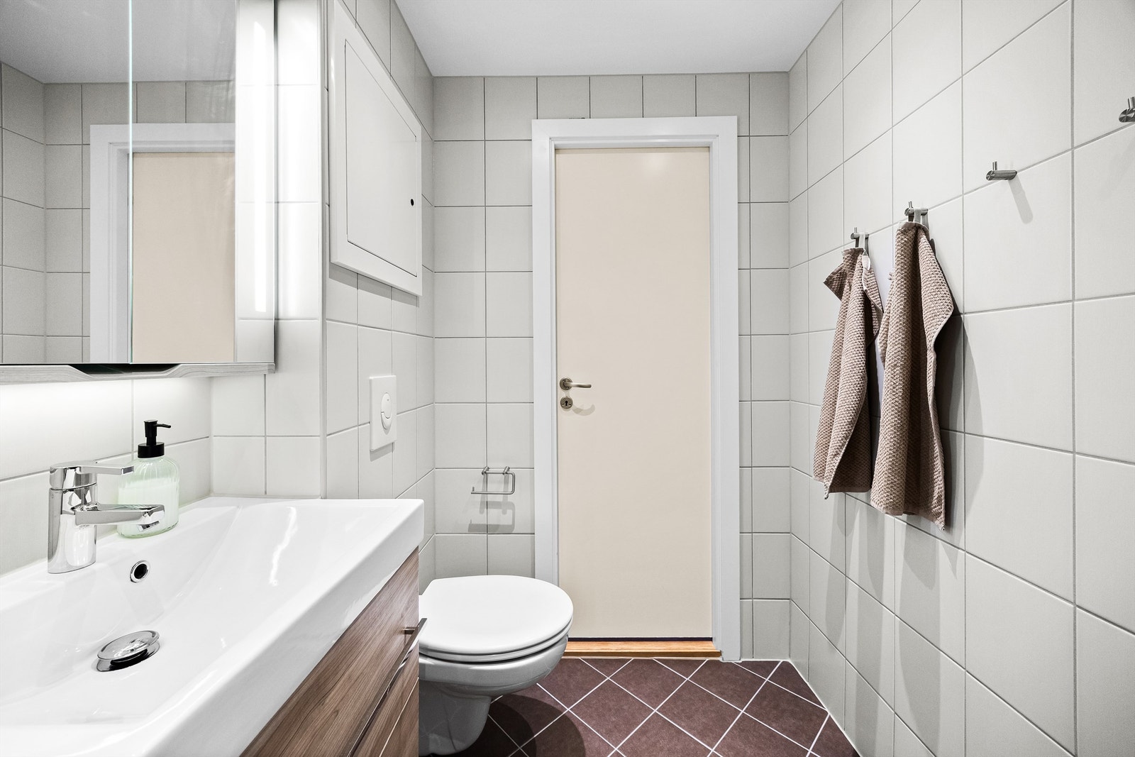 Badet består av dusjhjørne med glassdører, dusjarmatur tilkoblet hånddusj, vegghengt toalett, vegghengt servantinnredning med ovenpåliggende servant og armatur, speilskap med belysning og stikkontakt på vegg over servant Galleribilde