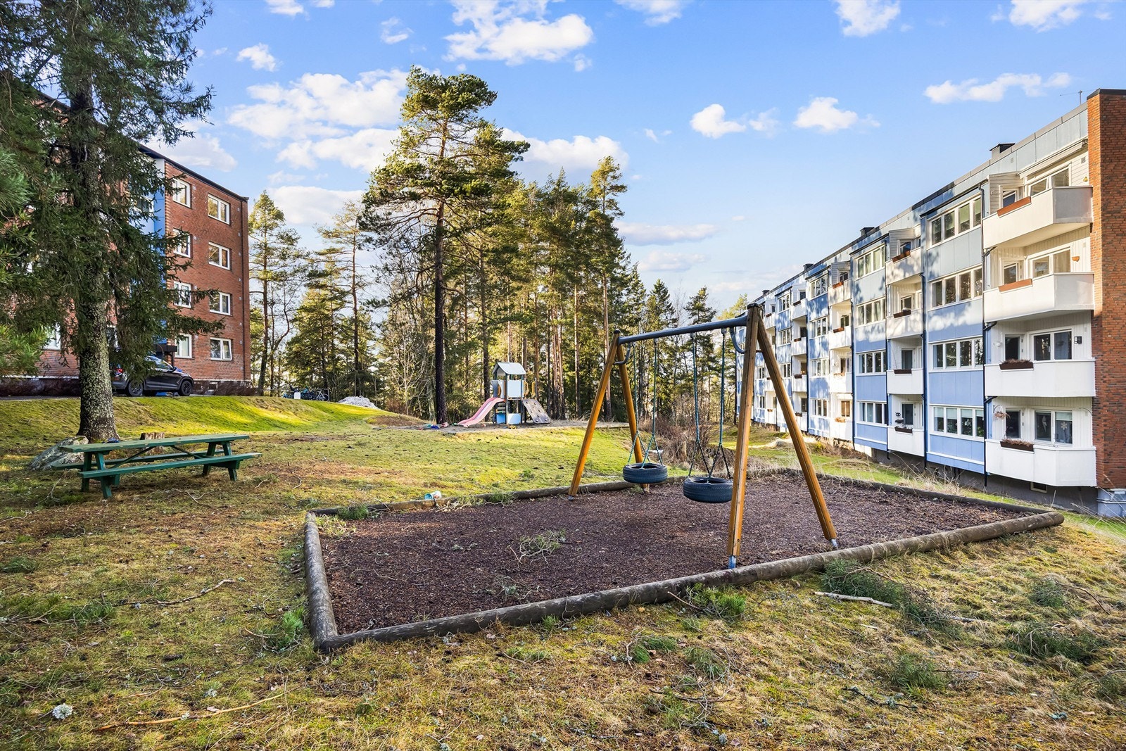 Felles festet tomt opparbeidet med blant annet asfalterte internveier, biloppstillingsplasser, lekeapparater, sittebenker, gressplen, trær og diverse beplantning Galleribilde