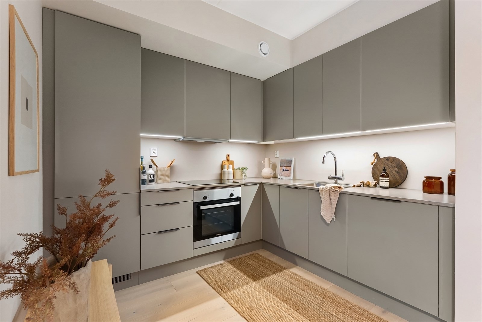 Laminat benkeplate med nedfelt stålkum og induksjonstopp, med led lys under overskap som lyser opp benkeplaten. Integrerte hvitevarer består av komfyr, oppvaskmaskin og kombindert kjøeskap/fryser. Det er avtrekk via balansert anlegg. Galleribilde