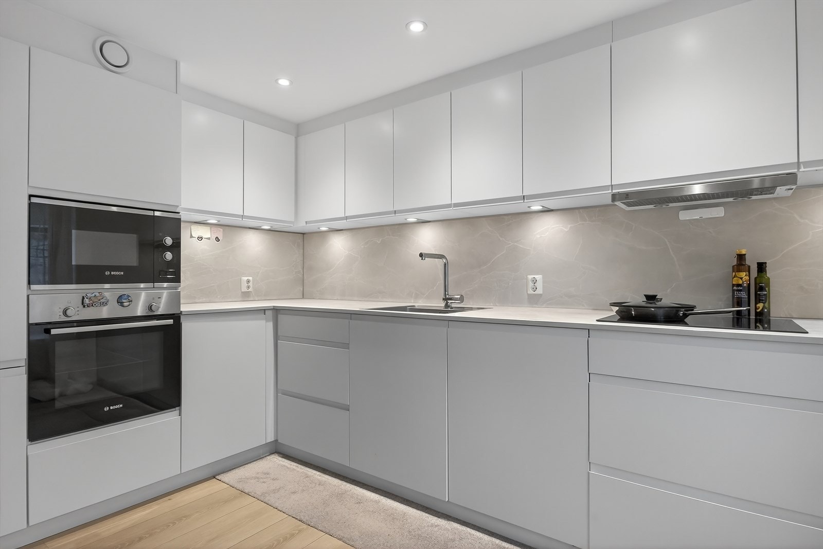 Kjøkkenet fremstår stilrent med glatte fronter, og integrerte hvitevarer i arbeidshøyde gir både moderne uttrykk og praktisk bruk. Galleribilde