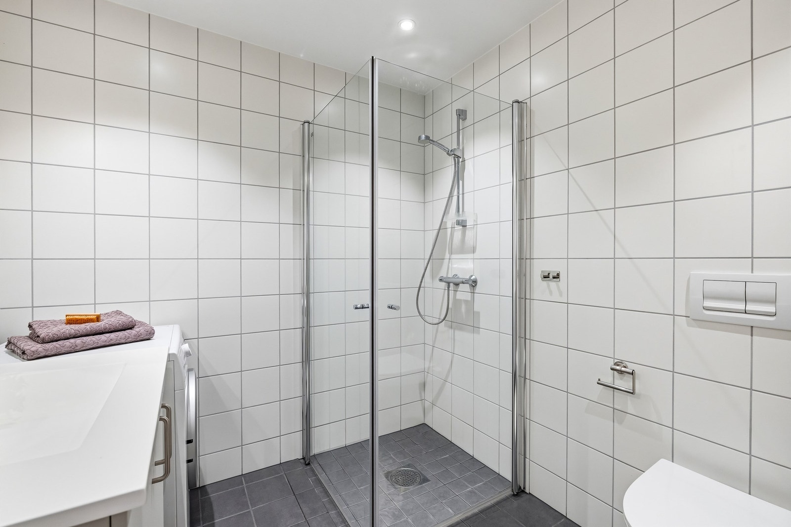 Dusjhjørne med innfellbare glassvegger, vegghengt toalett, samt opplegg for vaskemaskin. Galleribilde