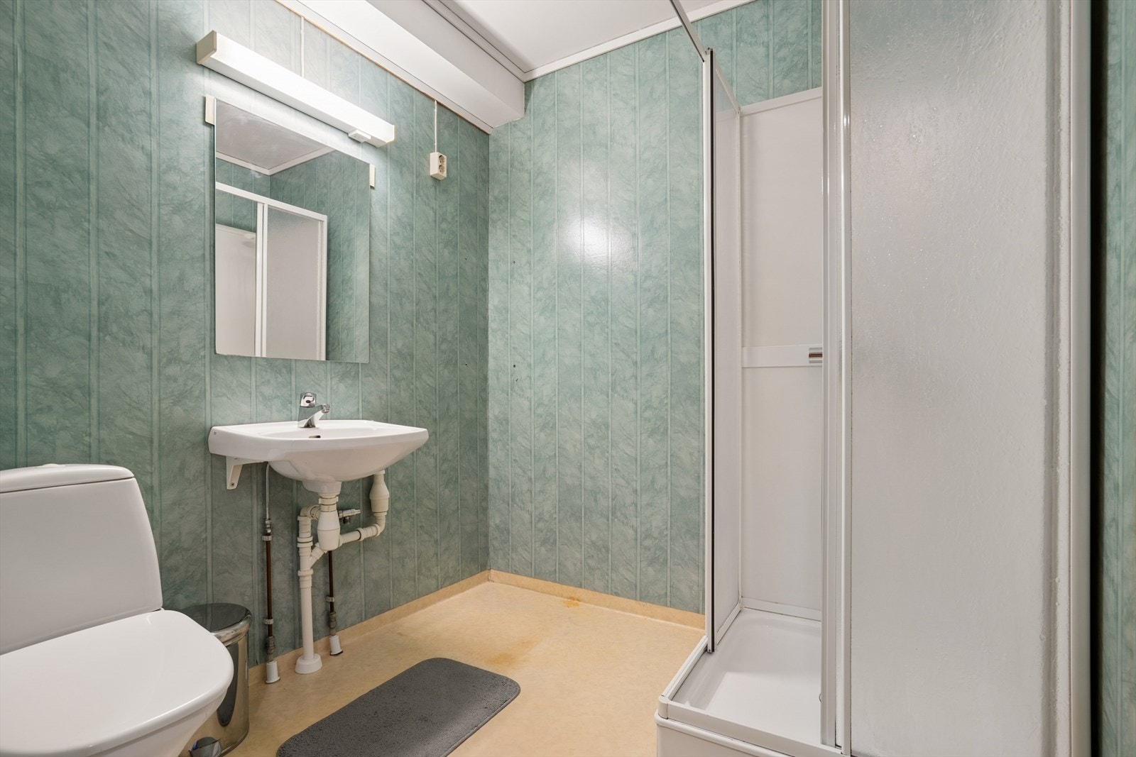 Badet har gulvbelegg og tapet på vegger (oppgradering bør påregnes) - Her finner du toalett, dusjkabinett og servant på vegg Galleribilde