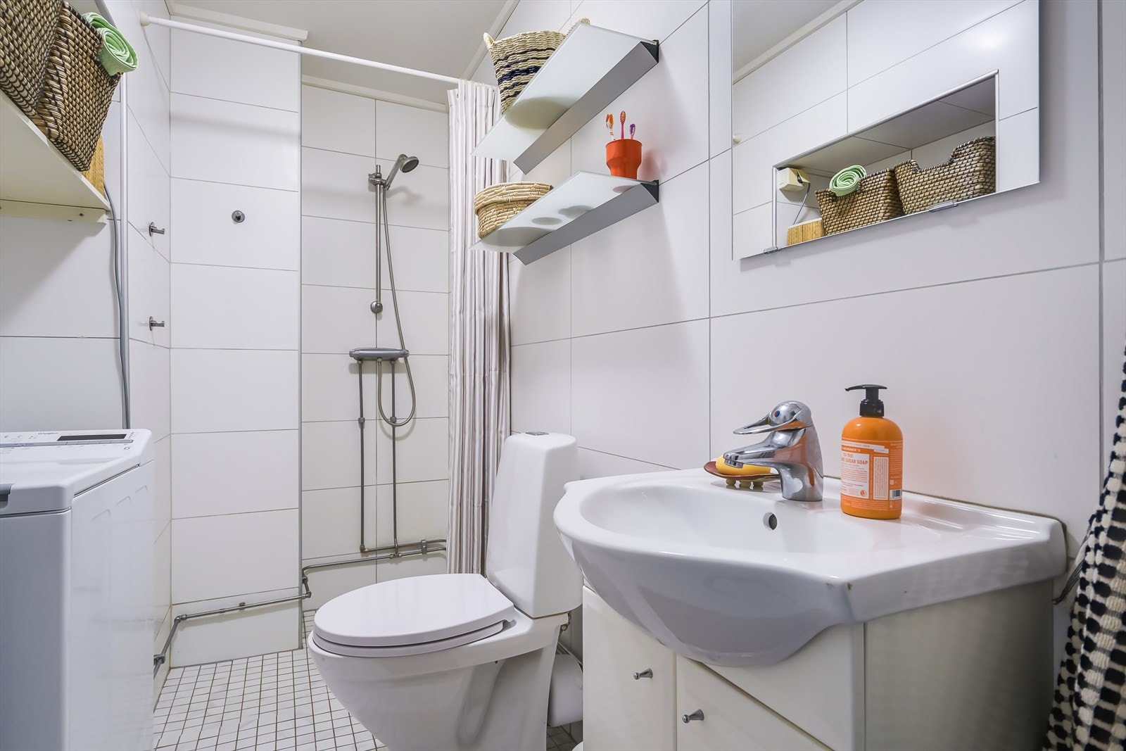 Lyst flislagt bad fra 2009 innredet med servant, klosett, dusjhjørne og opplegg for vaskemaskin. Galleribilde