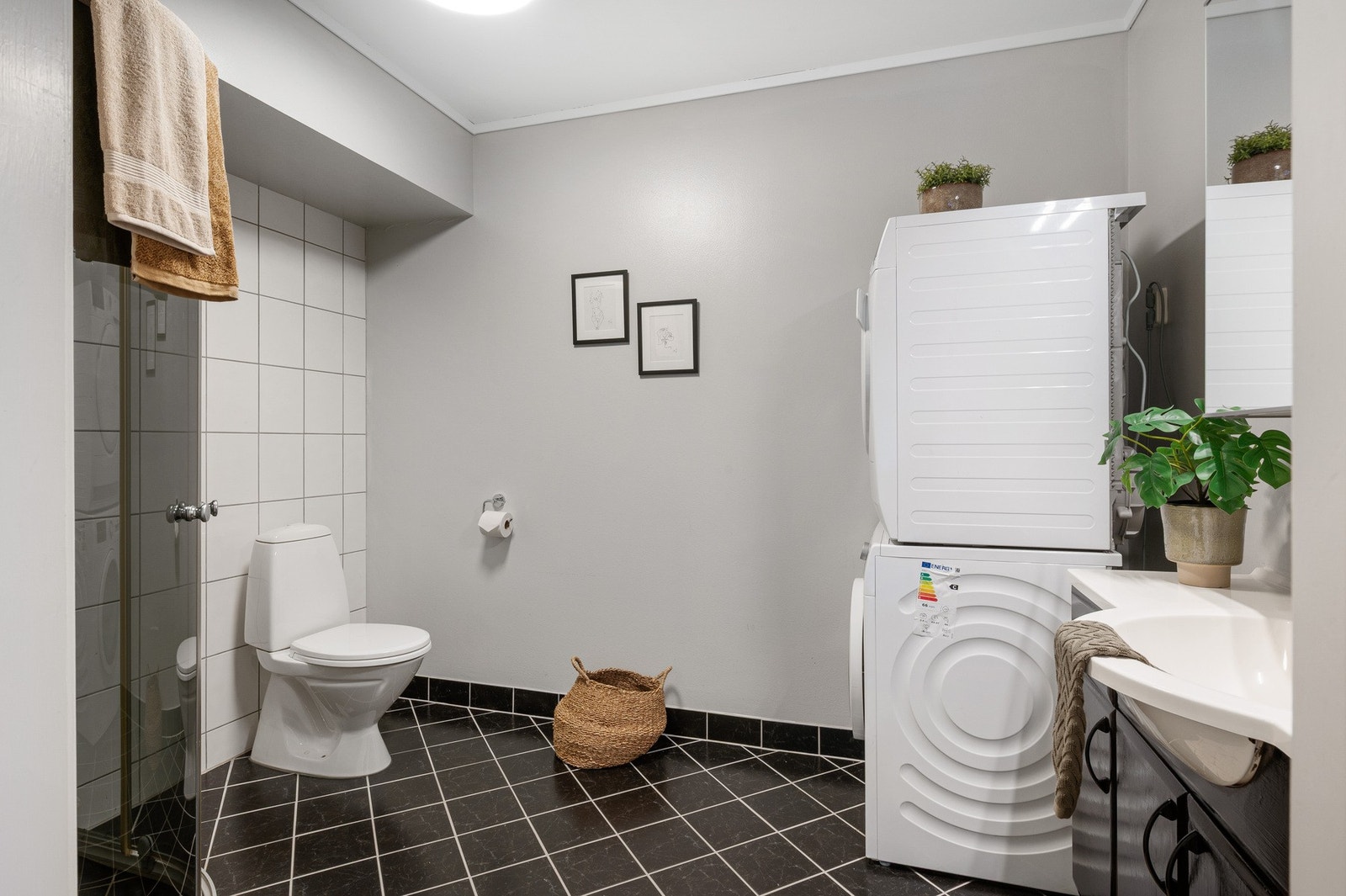 Badet inneholder toalett, helstøpt servant, skap under servant med slette fronter, dusjdører i klart glass, og opplegg for vaskemaskin. Galleribilde