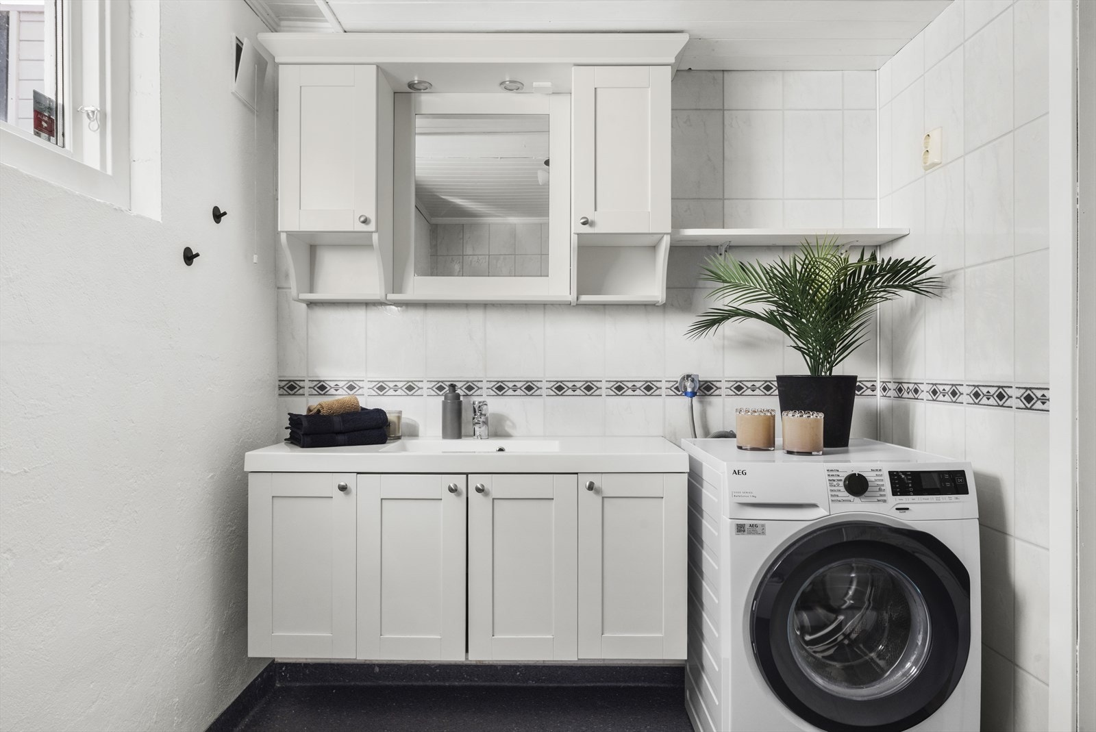 Badet er utstyrt med servant over skapinnredning, speil med vegghengt sideskap, toalett, badekar og opplegg til vaskemaskin Galleribilde