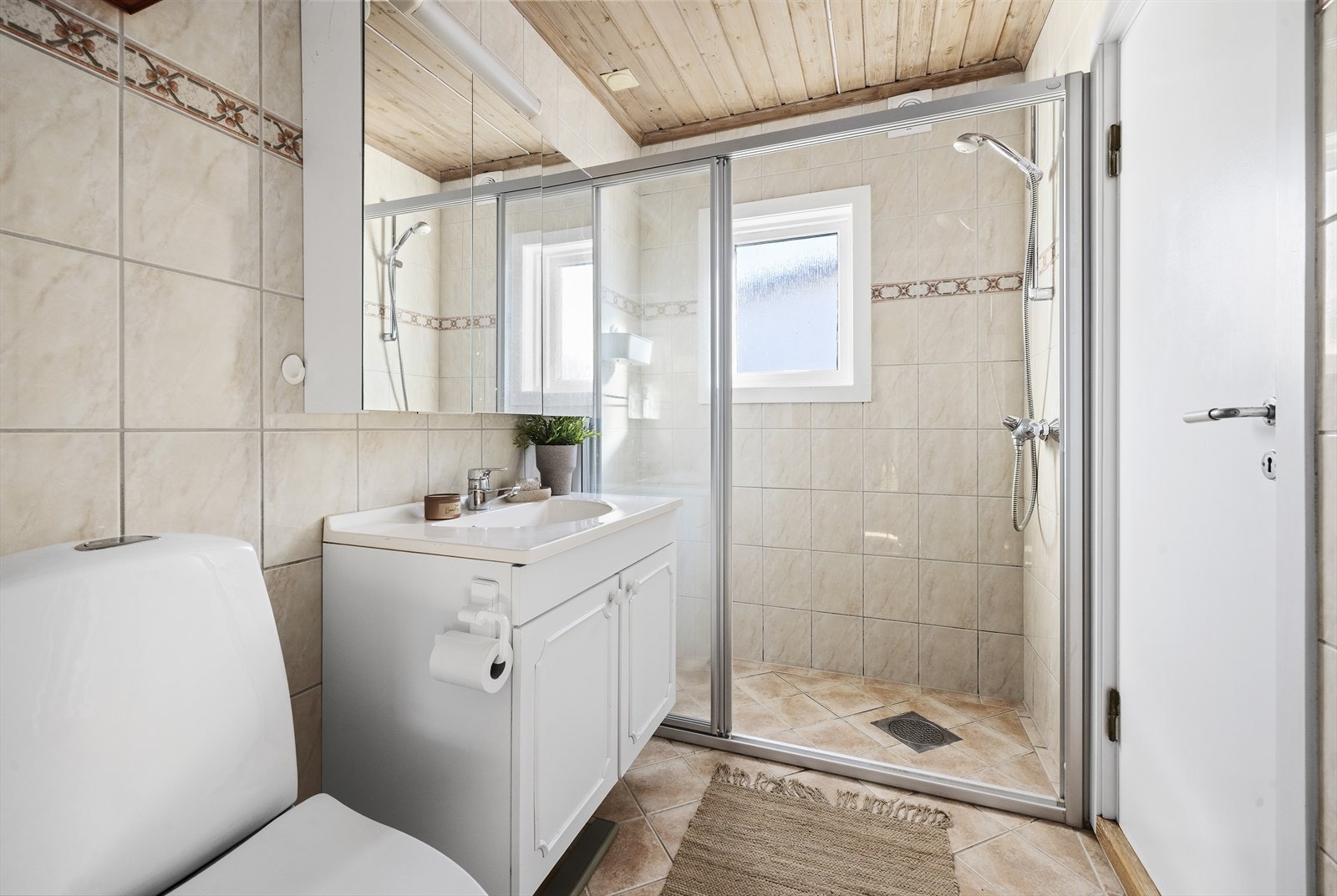 Helfliset baderom med varmekabler i gulv. Baderommet er utstyrt med servant over skapinnredning, speilskap, toalett og dusjhjørne Galleribilde