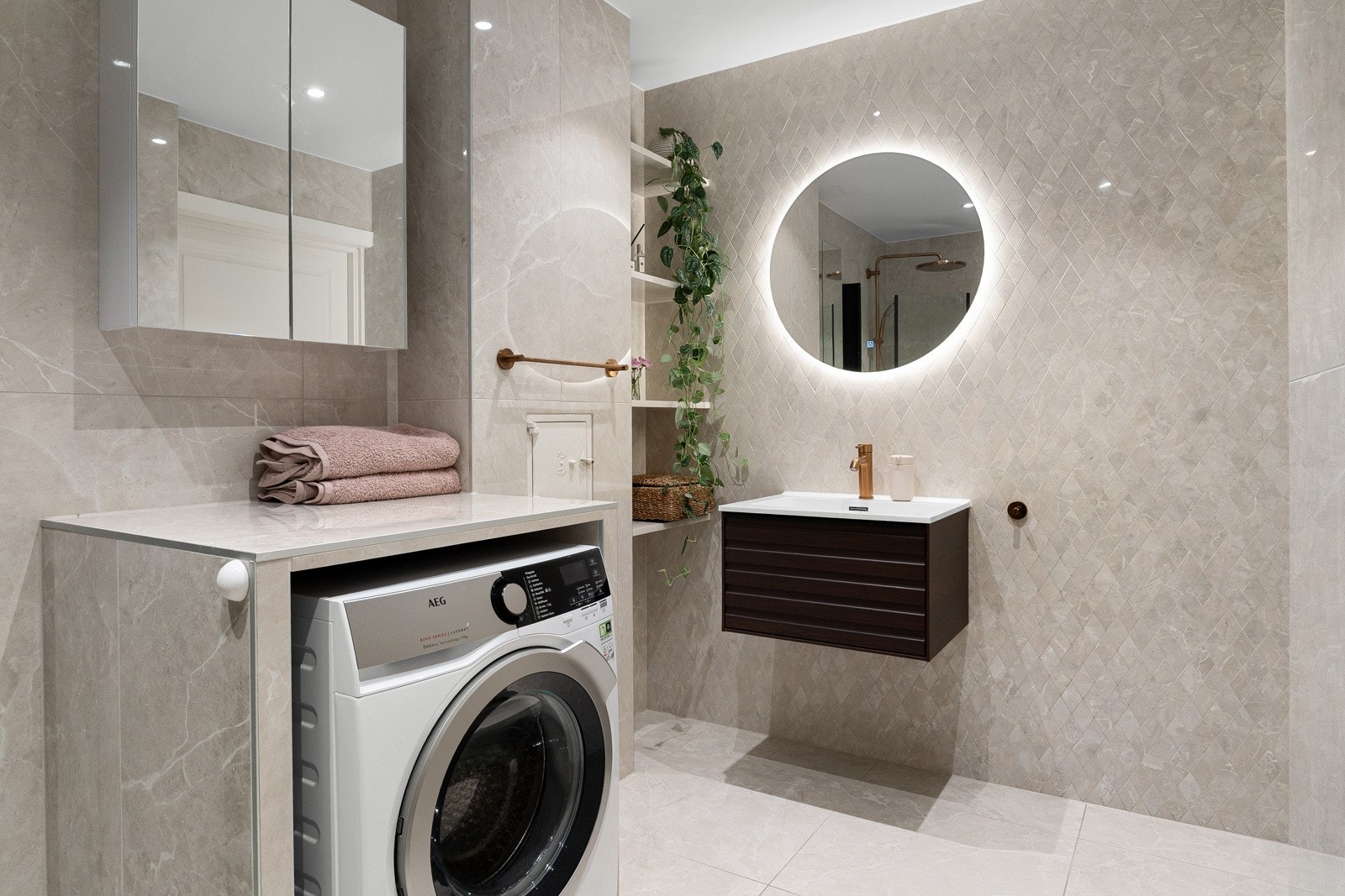 Veggmontert servantskap med heldekkende vask og ett-greps armatur i børstet messing. Opplegg for vaskemaskin i nisjekasse. Galleribilde