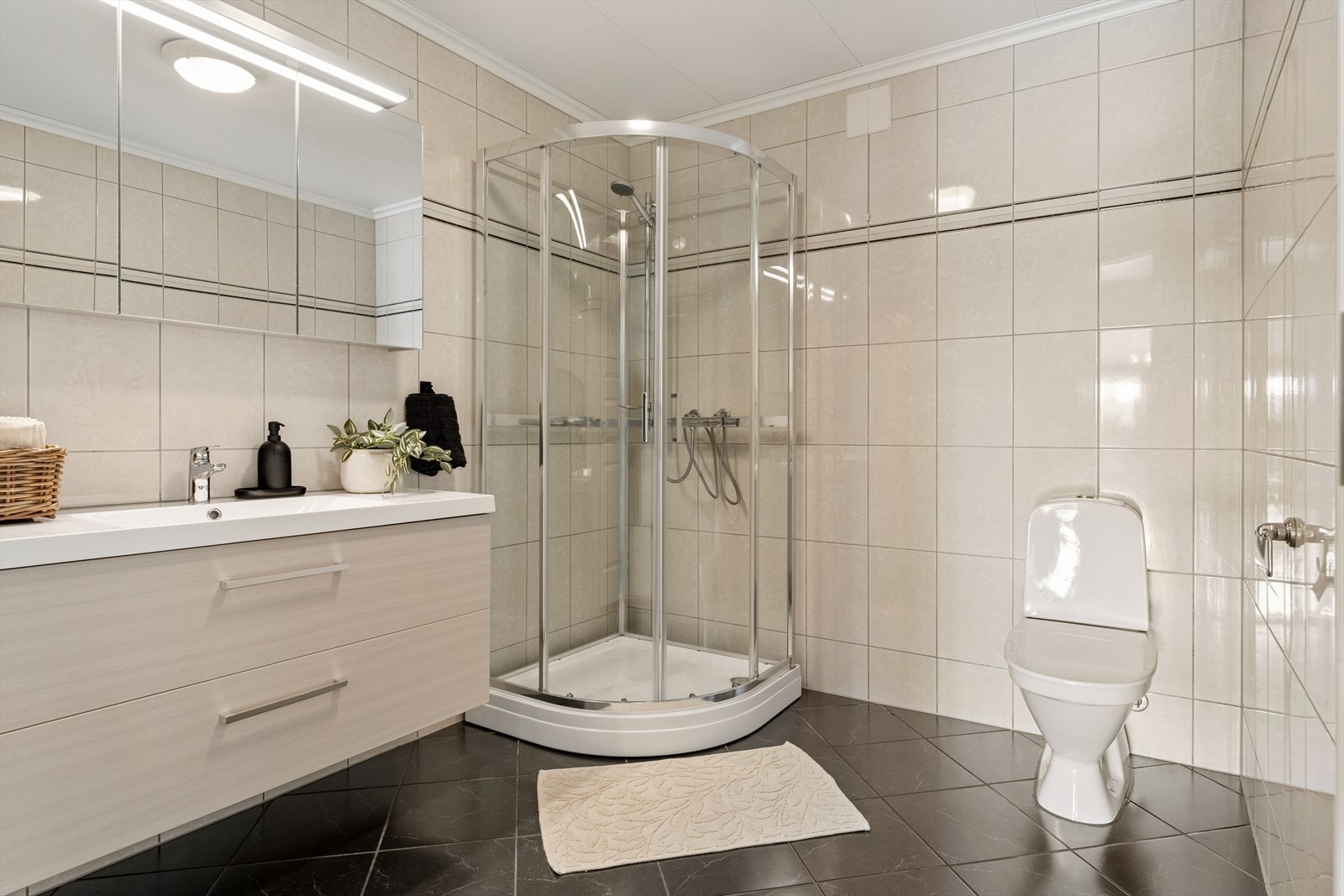 Badet fremstår som delikat og tidløst, med fliser i behagelige beige toner som gir rommet et varmt og harmonisk uttrykk Galleribilde