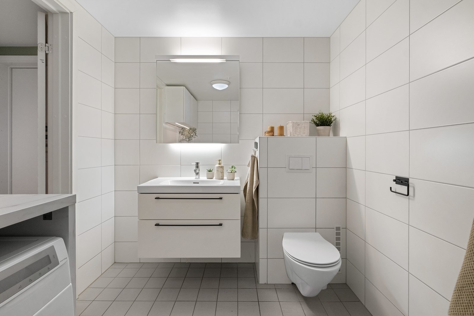 Flott flislagt bad utstyrt med veggmontert wc, servant med servantskap, speil med belysning og dusj med glassdører og regnfallsdusj Galleribilde