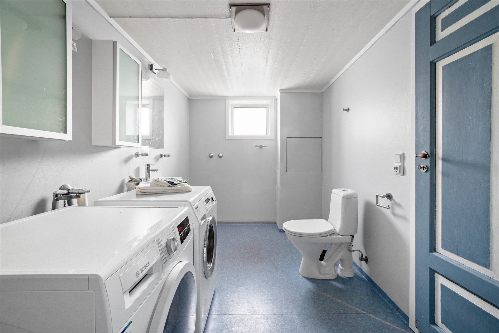 Stort og praktisk vaskerom i kjelleren med vinylbelegg og varmekabler. Veggene ble malt med våtromsmaling i 2025. Galleribilde