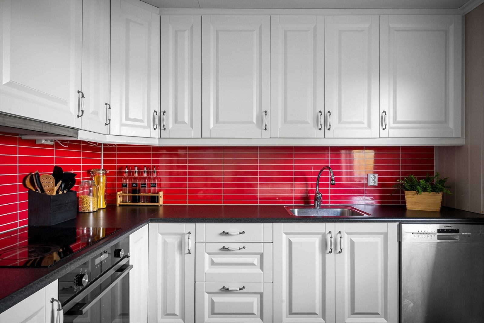 Innredningen har profilerte fronter i hvitt, kombinert med røde fliser som en delikat kontrast. Benkeplaten er av slitesterk laminat, og kjøkkenet er fullt utstyrt med kjøl/fryseskap, oppvaskmaskin, platetopp og stekeovn. Galleribilde