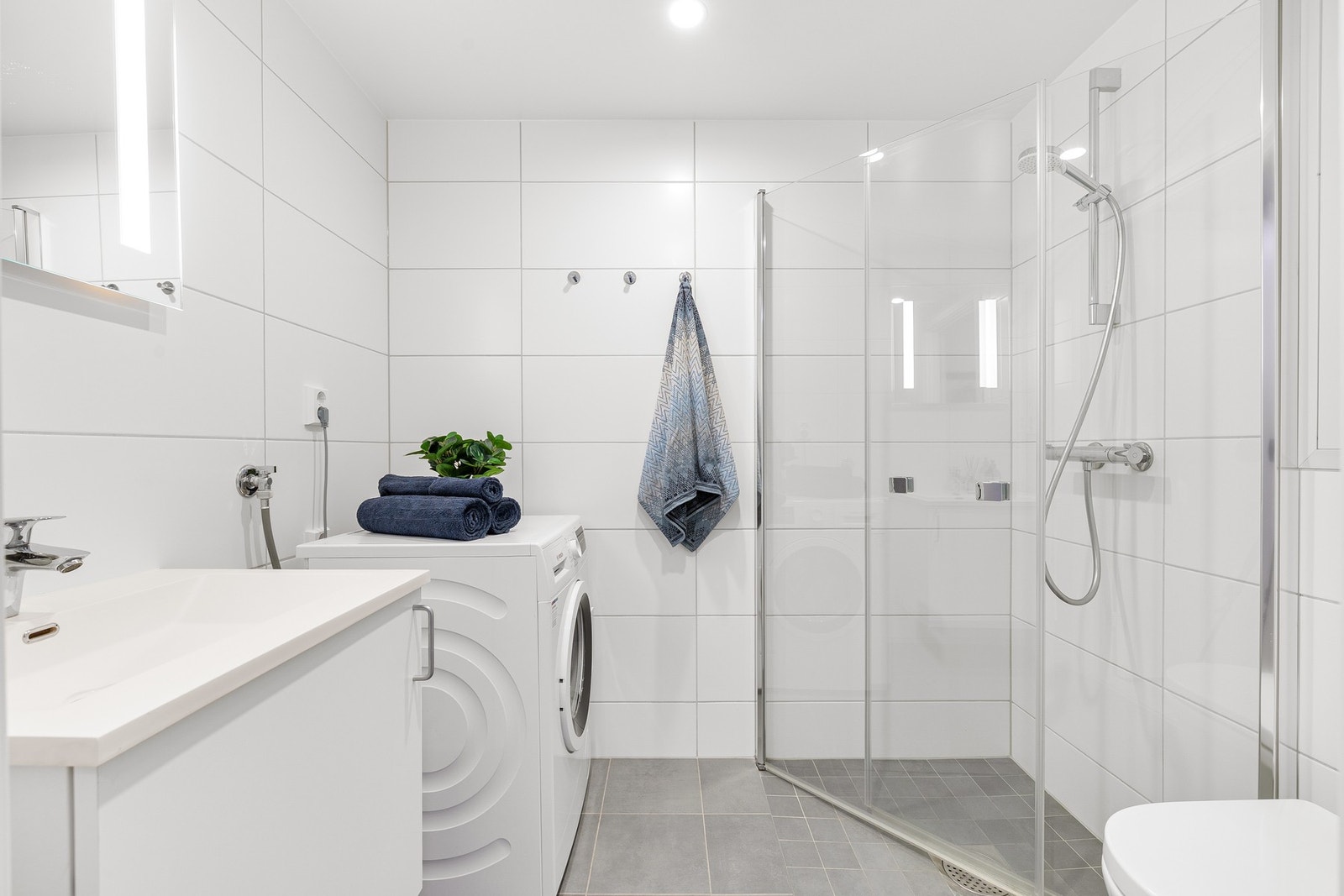 Baderommet med fliser på både gulv (elektriske varmekabler) og vegger holder i likhet med resten av leiligheten en høy standard med tildelt TG 0/1 av takstmann. Innehar innfellbare og plassbesparende dusjdører i glass, kran og avløp for vaskemaskin og veg Galleribilde