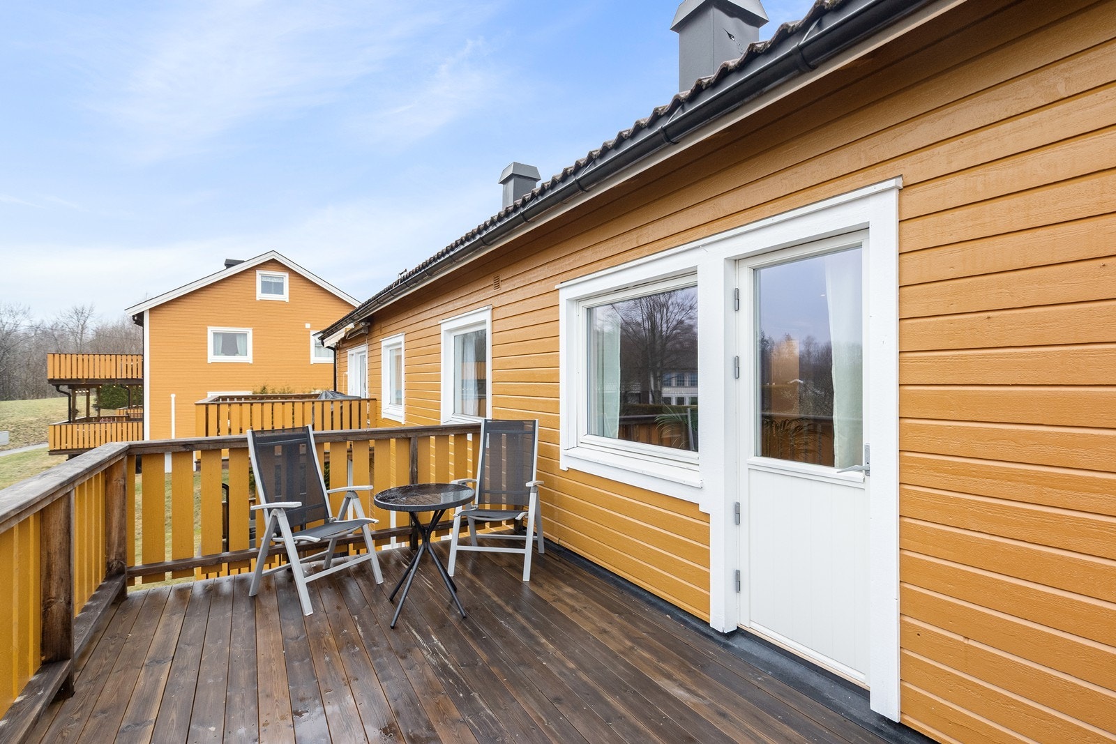 Utgang fra stuen til verandaen gir enkel tilgang til uteområdet, med malt trevirke på rekkverket. Galleribilde