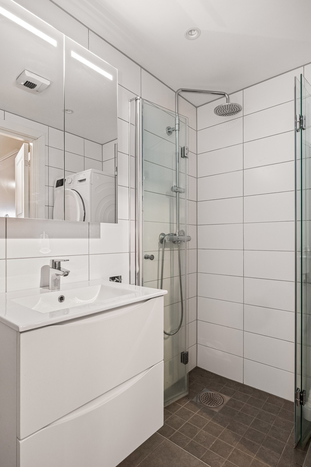 Her er det en nedsenket dusj med glassdører, downlights i taket og opplegg for vaskemaskin. Galleribilde