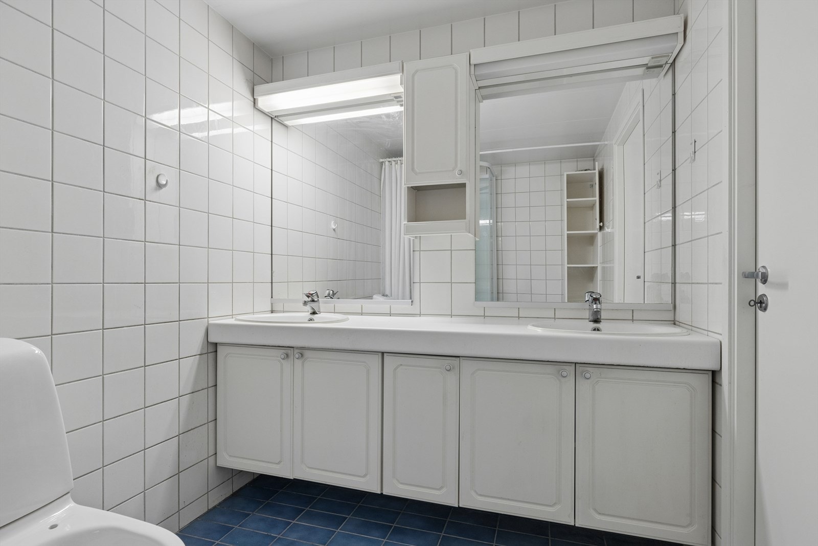 Badet i underetasjen har en gjennomførelse med dusjkabinett, klosett, dobbel servant med skapinnredning og to speil. Galleribilde